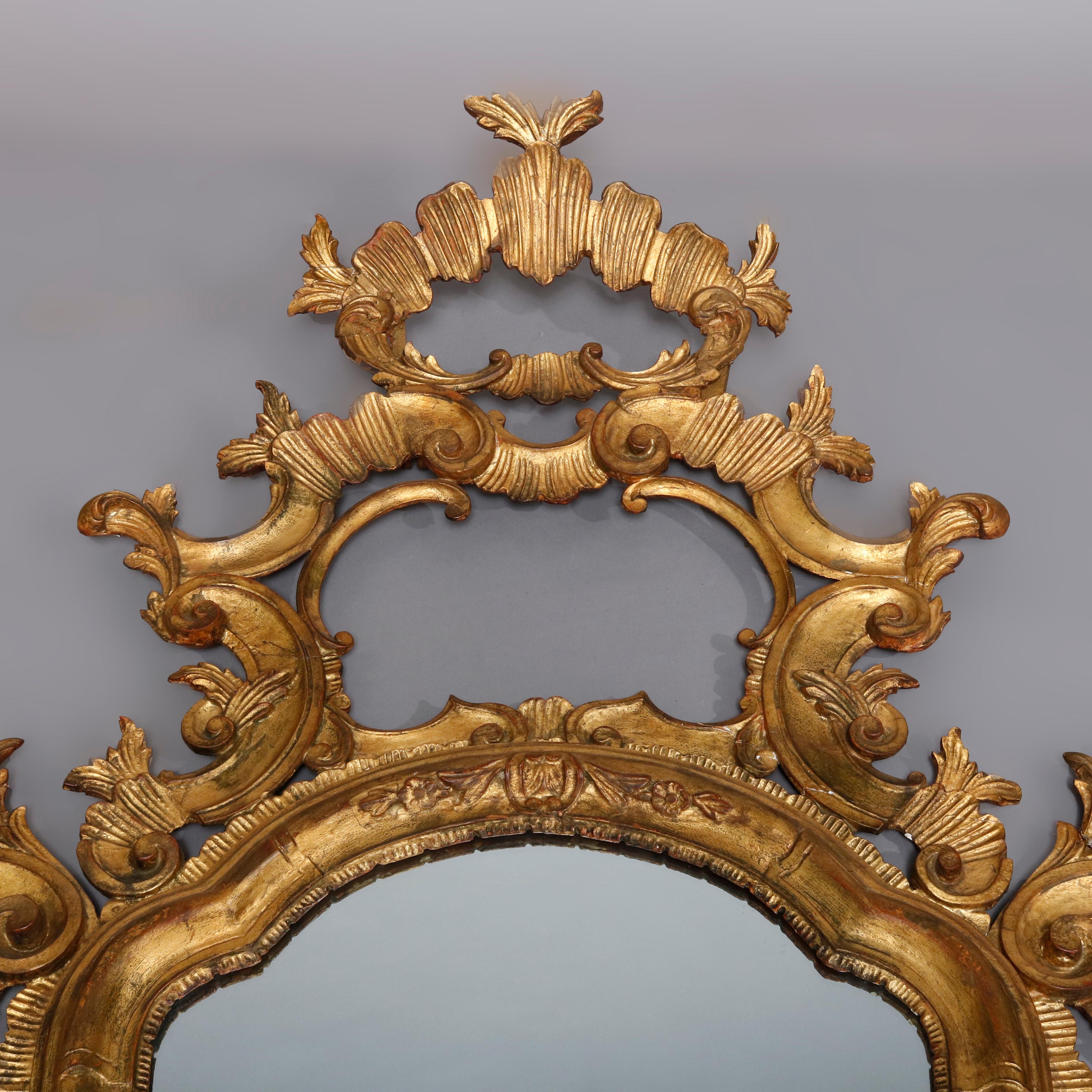 An antique pair of monumental 18th century Italian Baroque overmantel pediment mirrors offer finely sculpted giltwood frame having open foliate and scroll pediments surmounting arched mirror with pierced scroll and foliate elements throughout,