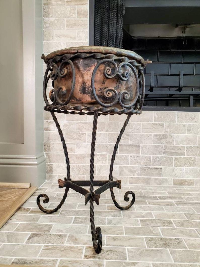 An antique wrought iron and copper planter, the later matched pair crafted from a late 19th / early 20th century stand and older primitive copper pot.

Hand forged in Italy, the black iron tripod plant stand finished in period Art Nouveau taste,