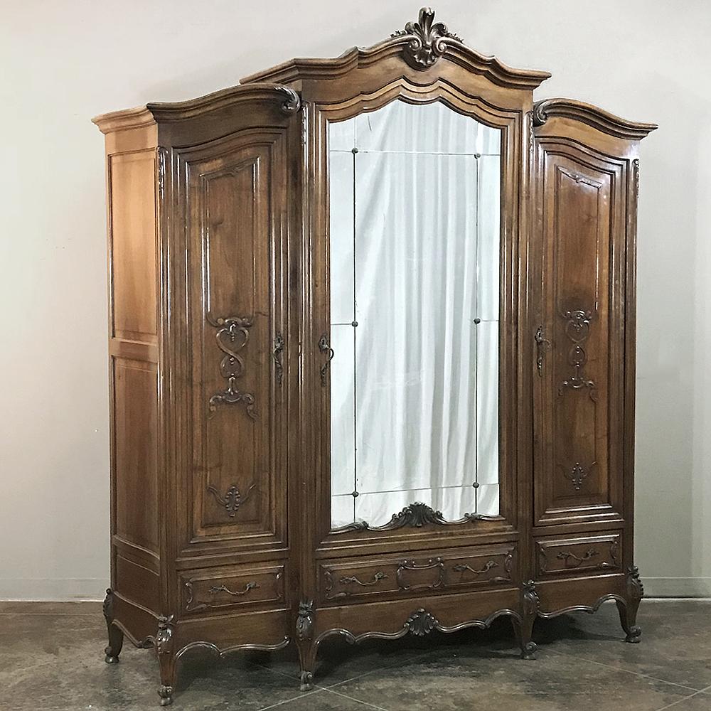 Antique Italian Baroque walnut triple armoire features a gracious Louis XV-influenced styling with triple crown design accented by step-front center section adorned with a Florentine fleur de lys atop the gracefully arched crown. Full length center
