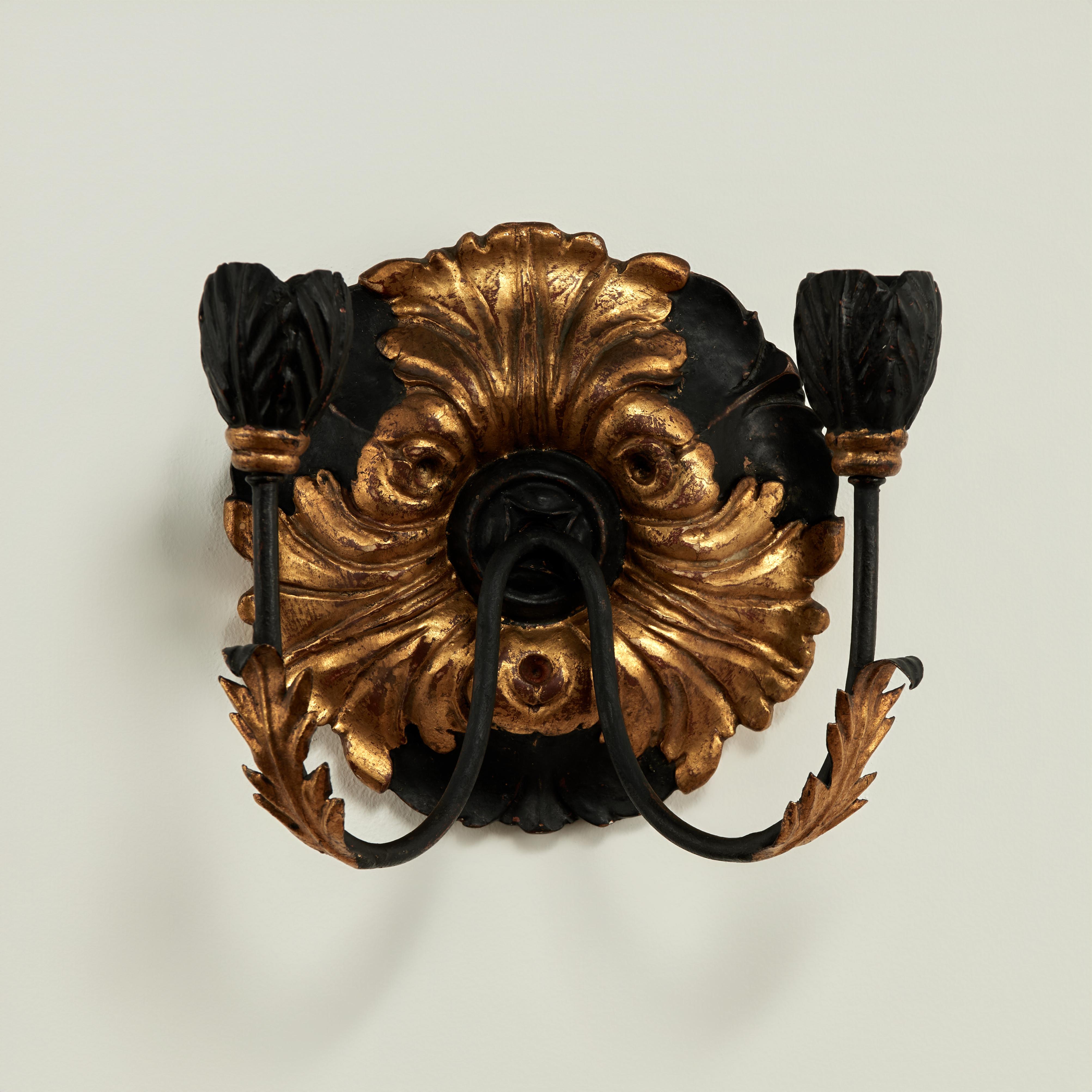 Applique a due luci in stile barocco con placca in legno intagliato con foglie d'acanto dorate su sfondo nero, due bracci in metallo con foglie dorate e coppe per candele floreali intagliate. Senza fili.