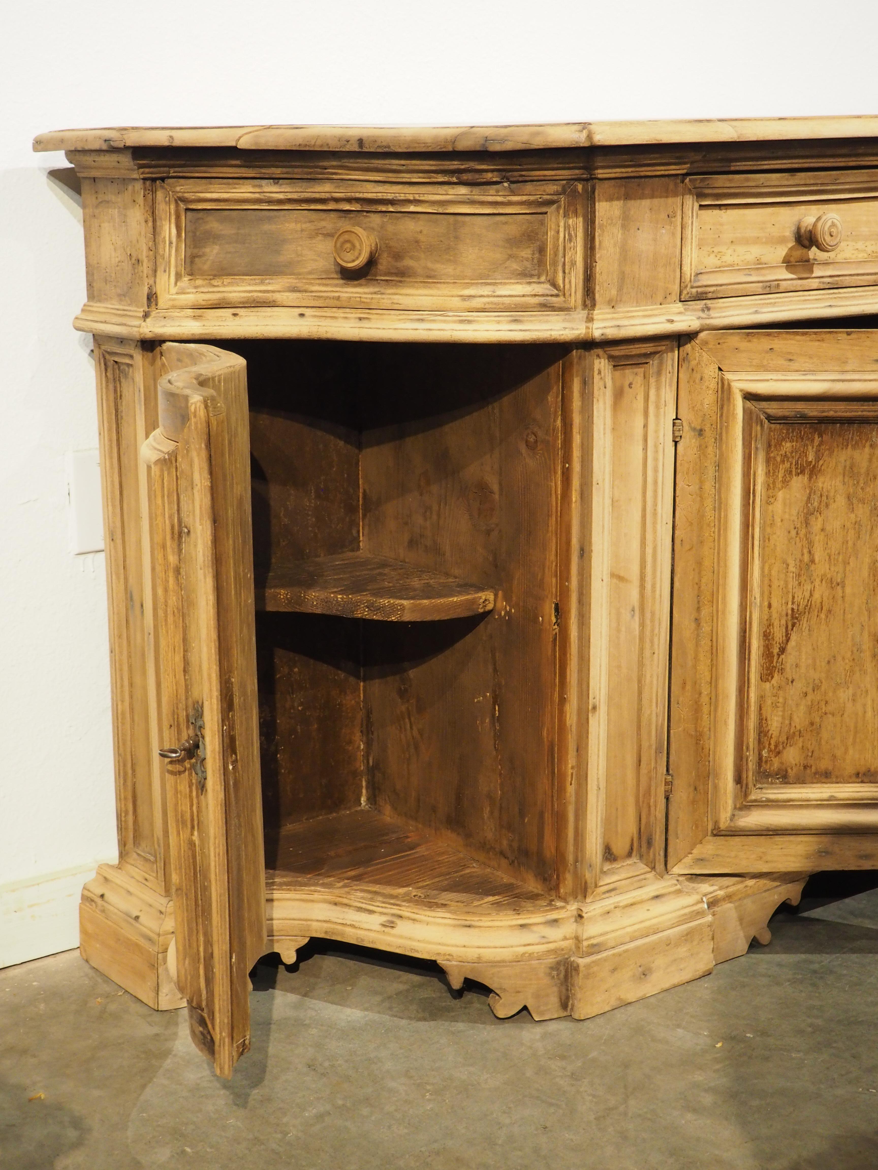 La forme sinueuse de cette crédence italienne en noyer blanchi respire l'élégance, en formant une arbalète presque complète. Sculptée à la main dans les années 1800, la crédence comporte trois compartiments, avec un segment central linéaire à double