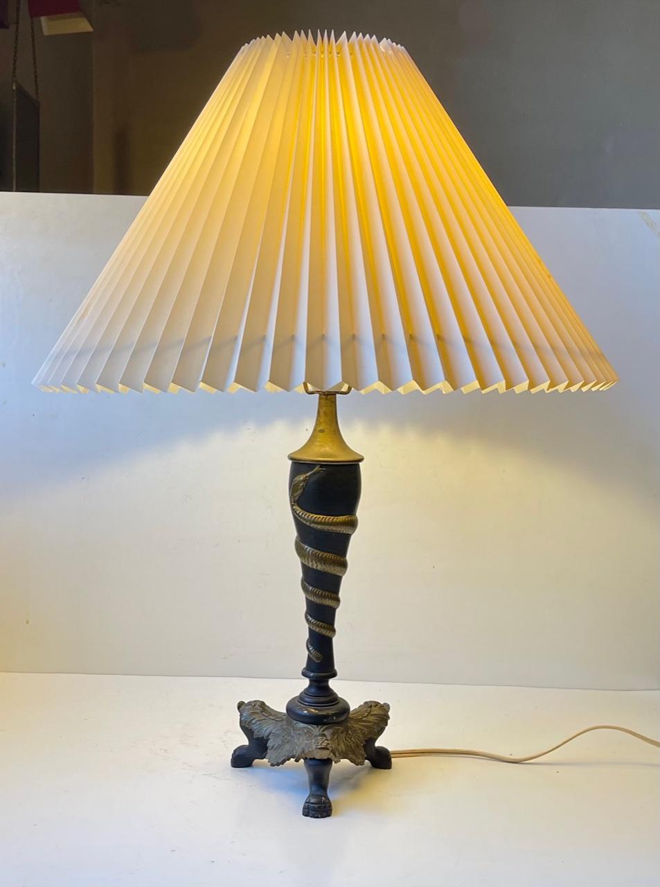 Ornate table lamp in brass. It features lions-feet and a twisted serpent in relief. It was made in Italy during the 1940s in a style inspired of E. Brandt. The on/of switch is located at the socket. Notice that the shade is not included. Please