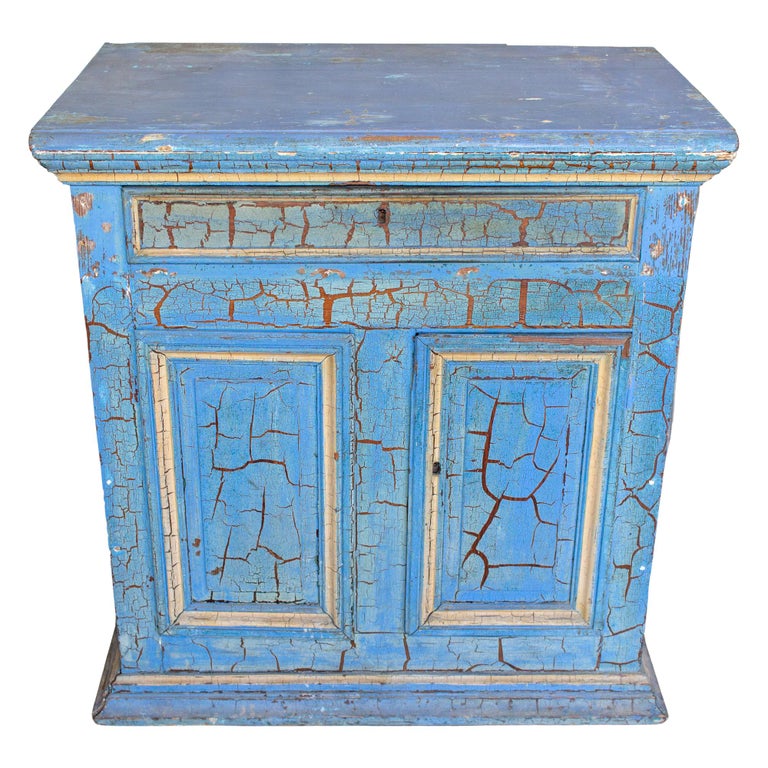 This very charming cabinet is antique Italian and has been finished in a crackling sky blue paint with gold accents. The cabinet has a wide top drawer and two lower doors which open to interior storage within. The front doors and each side are all