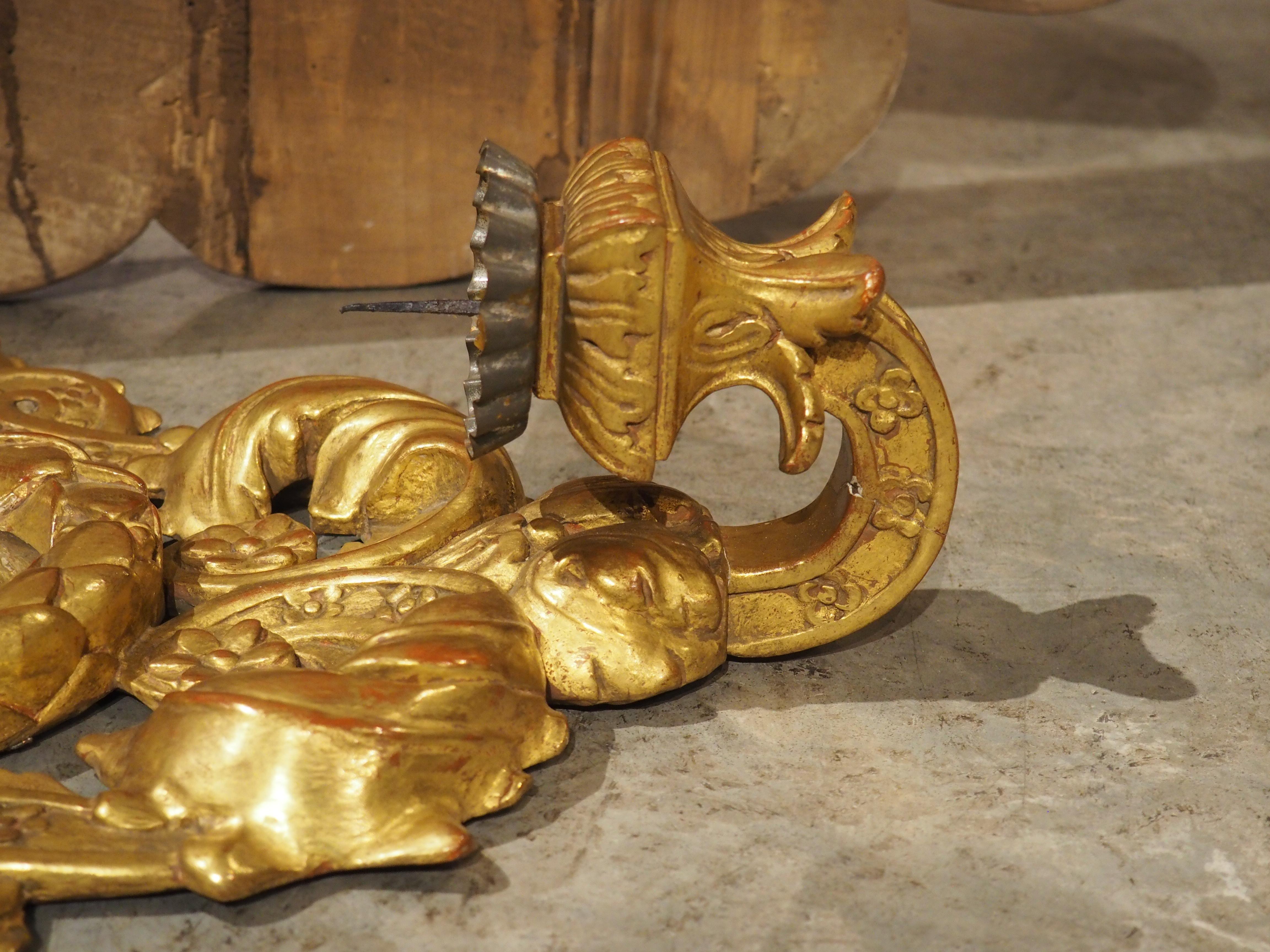 Sculptée à la main en Italie dans les années 1800, cette applique murale présente une vitrine brillante et dorée qui entoure un petit miroir ovale. Le miroir central est immédiatement entouré d'un anneau décortiqué surmonté d'une petite fleur.