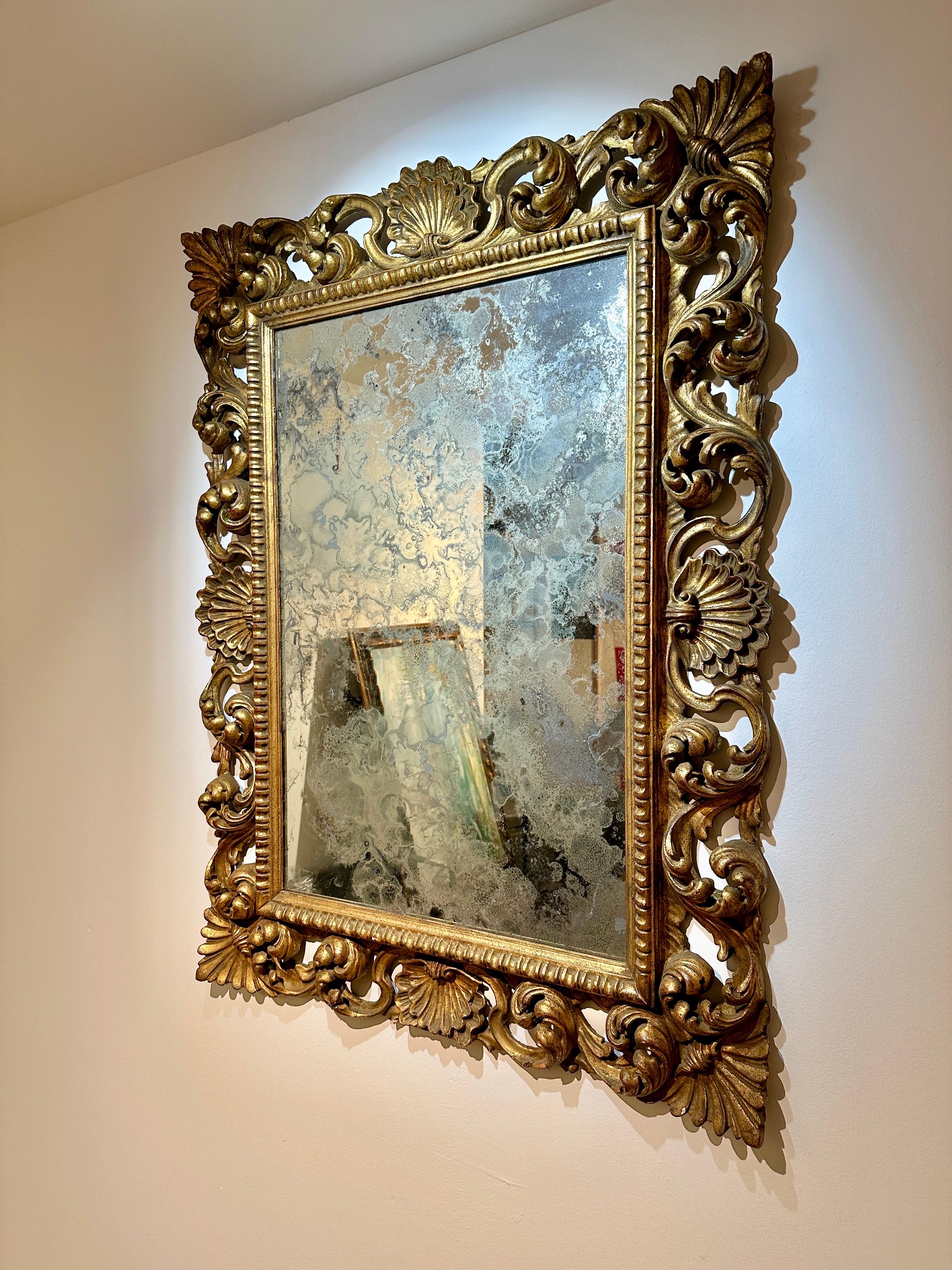 Antique carved giltwood frame flourished with seashells and details galore.  The antiqued mirror is aged.  The very bottom seashell has a few cracked pieces which can be seen up close, however, at a distance is very symmetrical.   