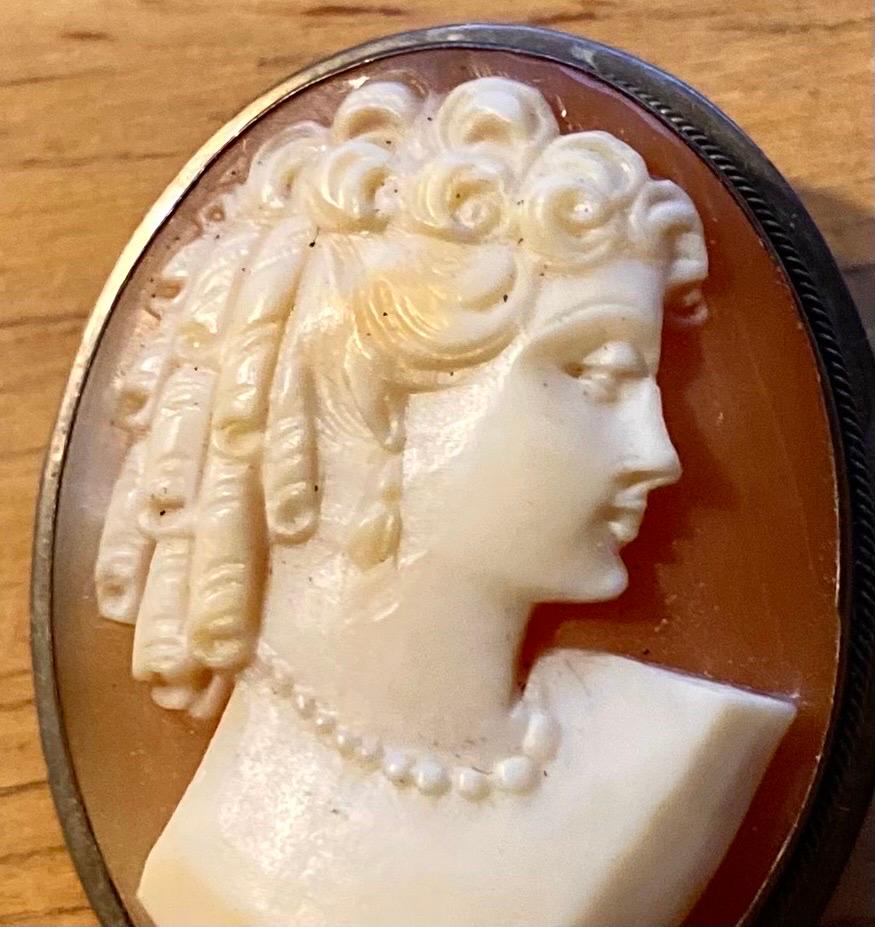 Late Victorian period Italian 900 coin silver hand carved shell cameo  brooch or pendant; the right facing young woman is wearing long barrel curls, or ringlets popular at the time. Cameo is set in a silver frame bezel. Swivel bail at the top for a