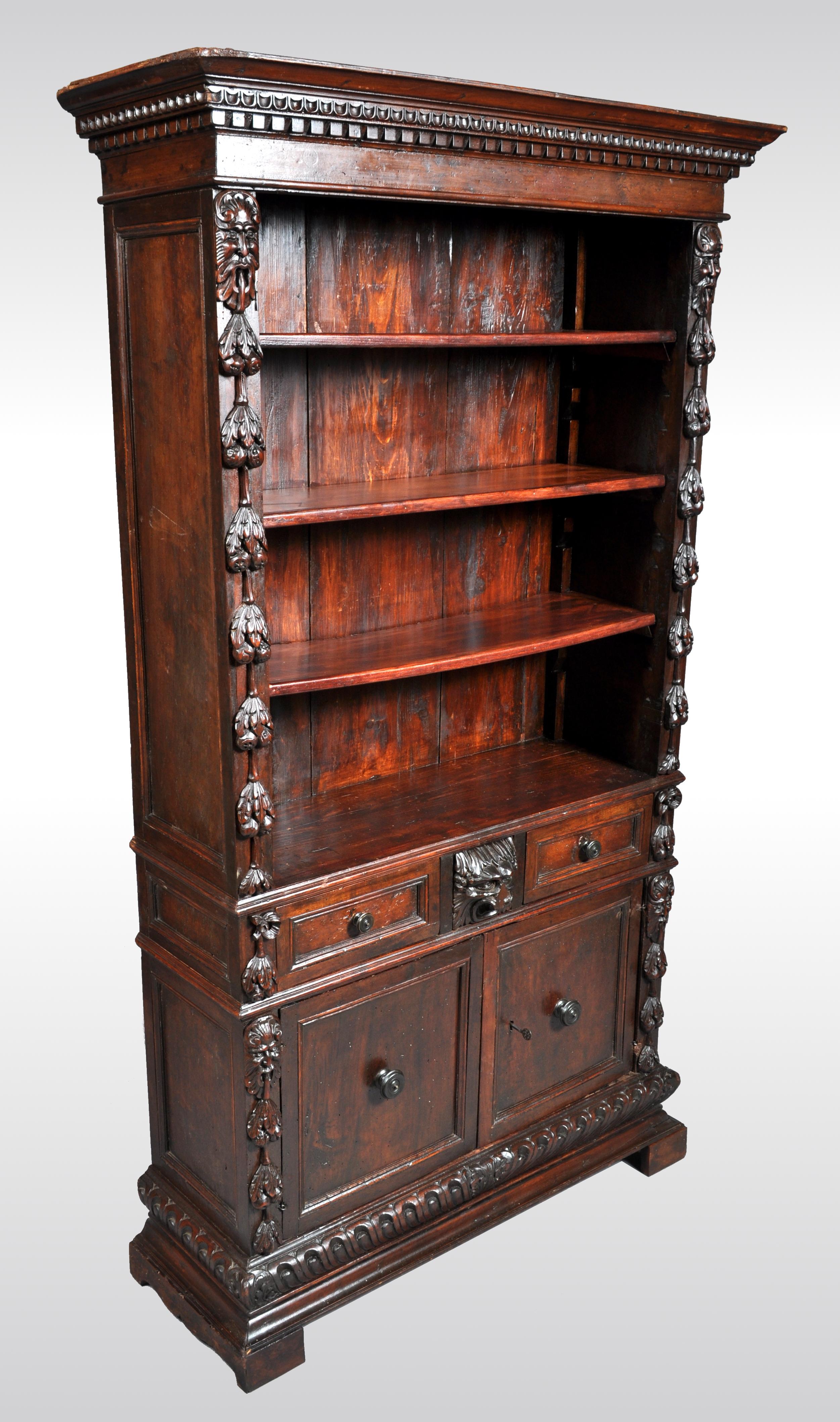 Antique Italian carved walnut renaissance revival bookcase, circa 1870. The bookcase having a protruding cornice with 'egg and dart' and dentil carving, the bookcase is flanked with carved fruits preceded by comical grotesque masks. The base having