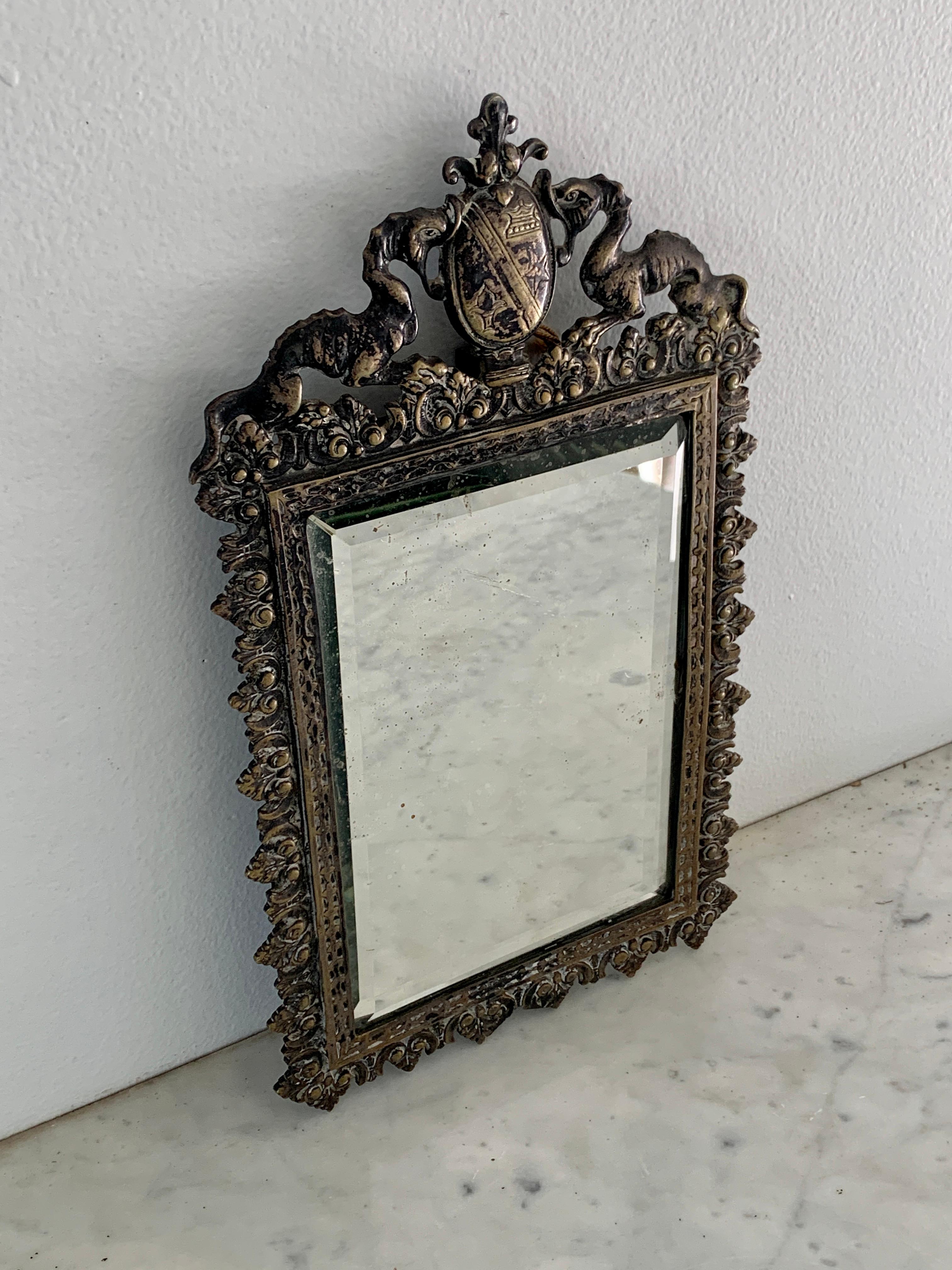 A stunning antique tabletop or wall mirror featuring two mythological dragons holding a coat of arms or family crest with a crown, star, and fleur-de-lis

Italy, Early 20th Century

Cast brass, with antique beveled mirror.

Measures: 7