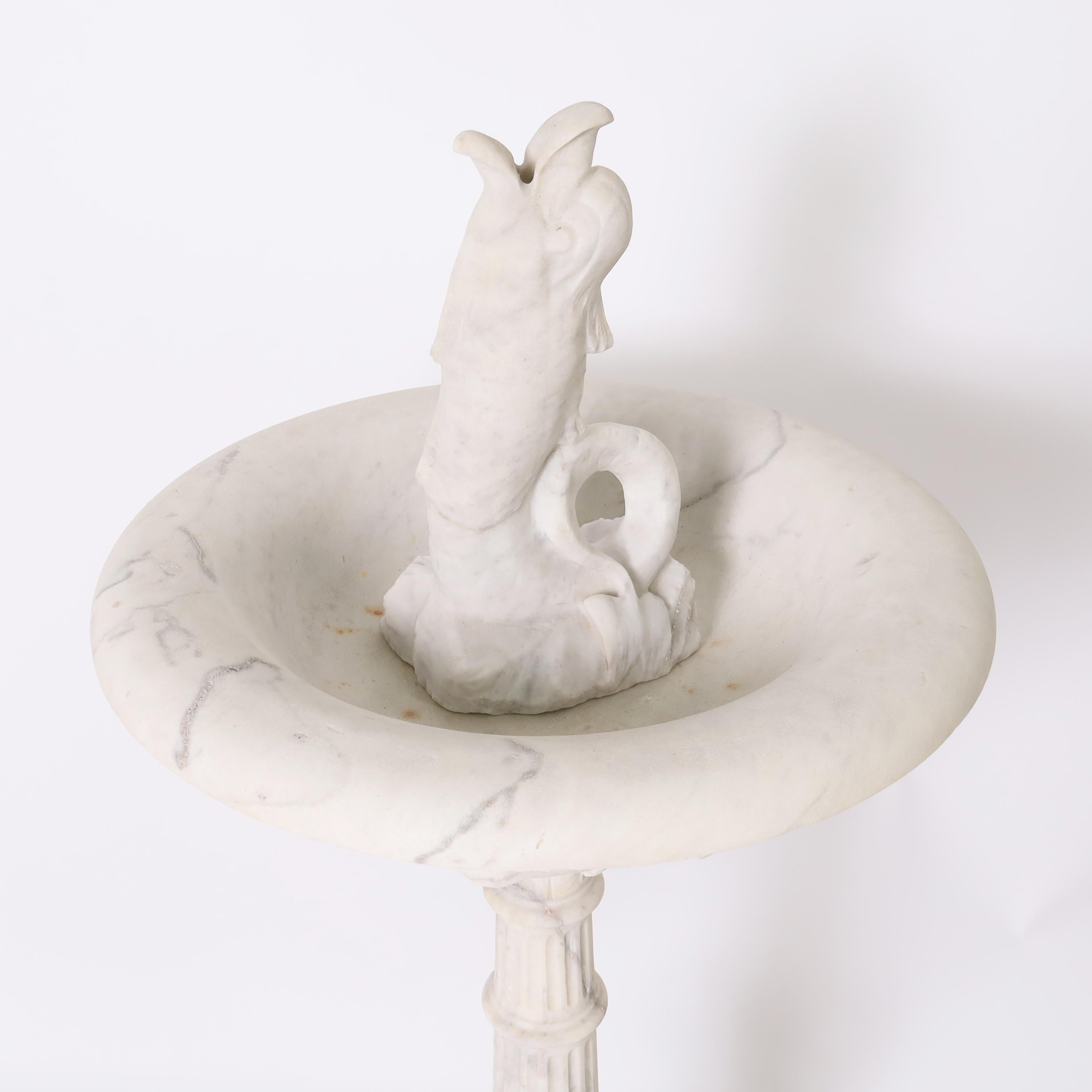 Impressionnante fontaine italienne néoclassique du XIXe siècle, sculptée à la main dans du marbre blanc, représentant un poisson mythologique dans une vasque ronde décorée de feuilles d'acanthe sur une colonne cannelée classique avec des feuilles,