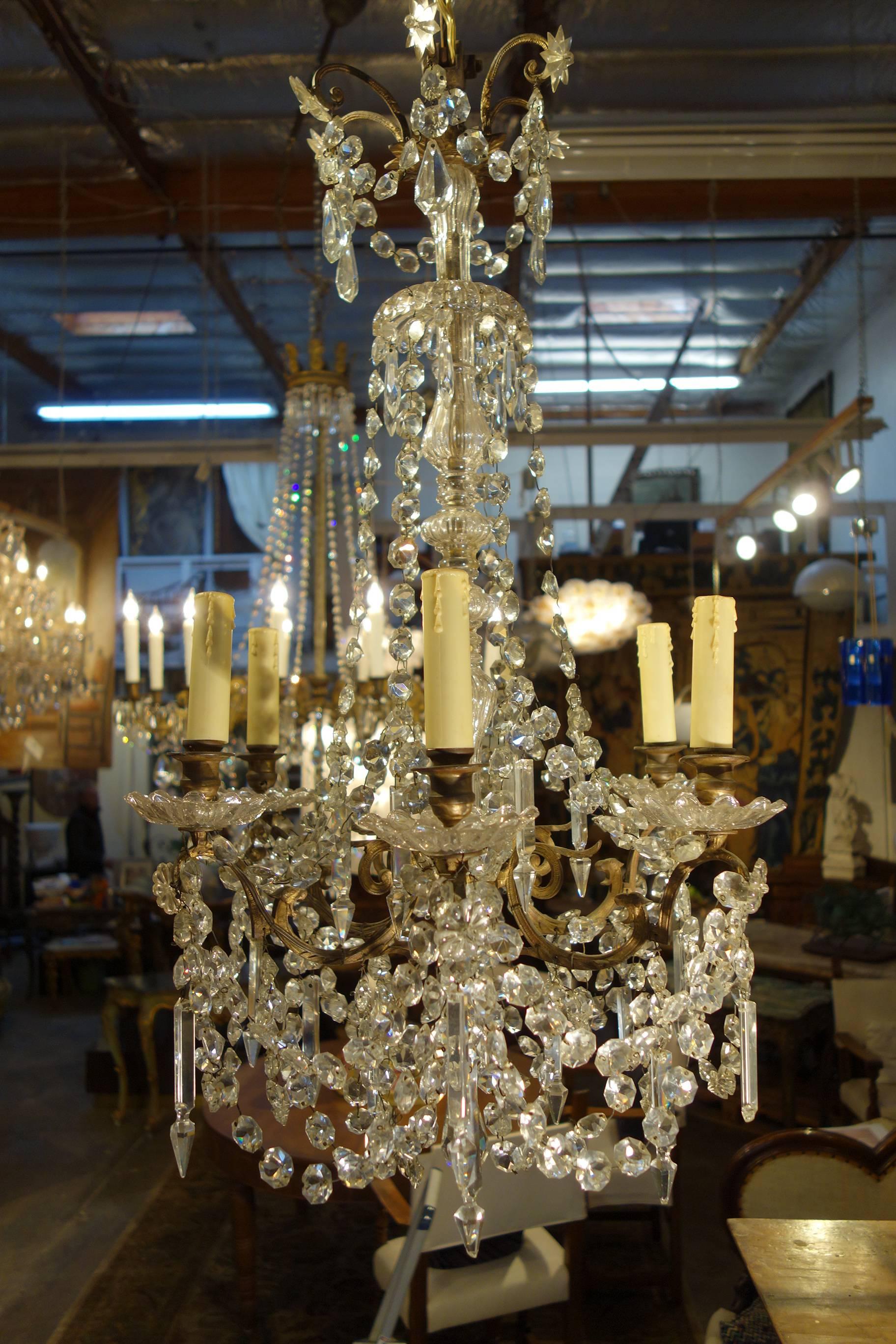 Elegant Empire style chandelier, opulent yet compact, featuring 6 crystal cups supported by delightful winged dragons on brass rocaille arms. Delicate, faceted glass beads, baubles and strands surround the central glass column.
Measures: 32