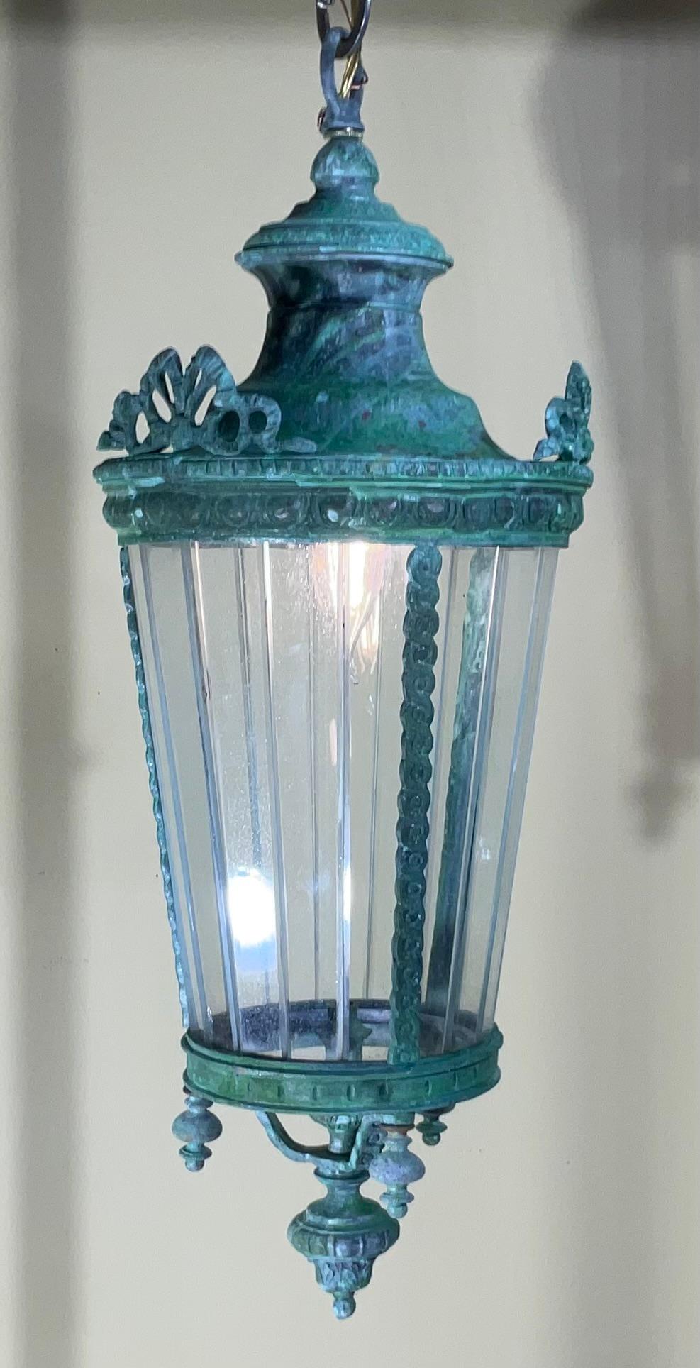 Elegante lanterne antique artistiquement forgée à la main  de bronze et de laiton, une lampe de 60 watts, des plaques de verre décoratives tout autour.
Belle patine.
Chaîne et auvent inclus.
