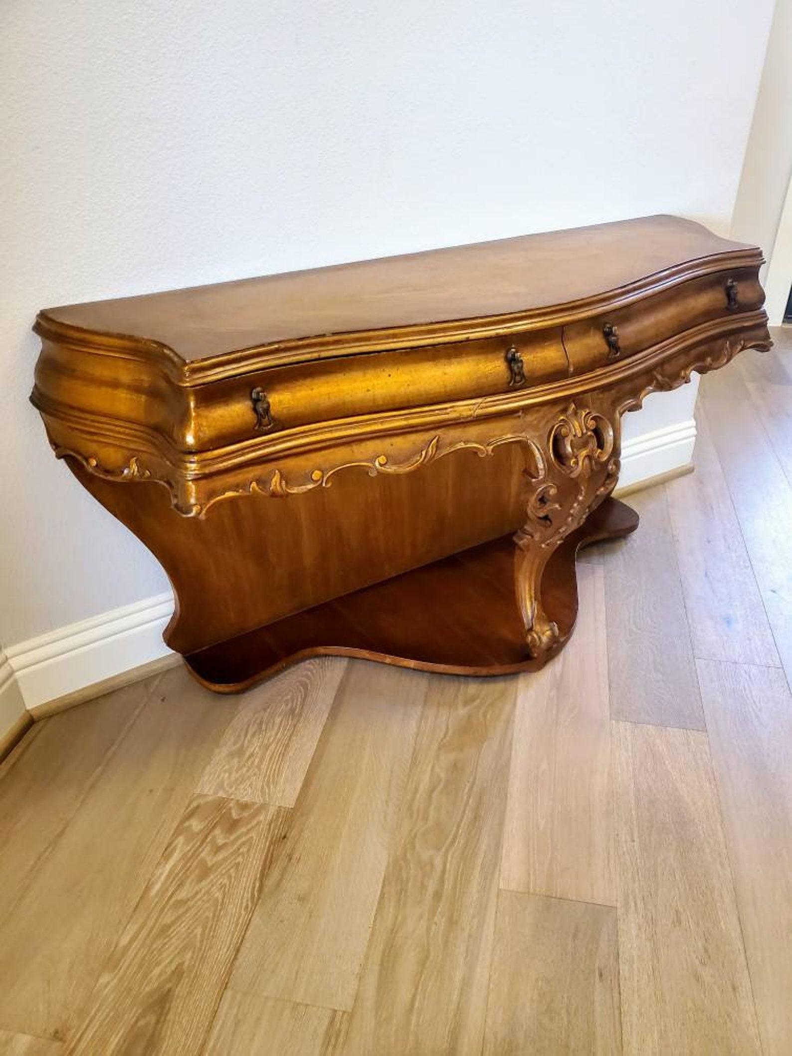 A rare and a little unusual carved gilt wood console table from the early 20th century.

Hand-crafted in Italy, solid wood construction, distressed painted gold lacquered gilded bronze finish, unique shapely bombe form, having a serpentine shaped