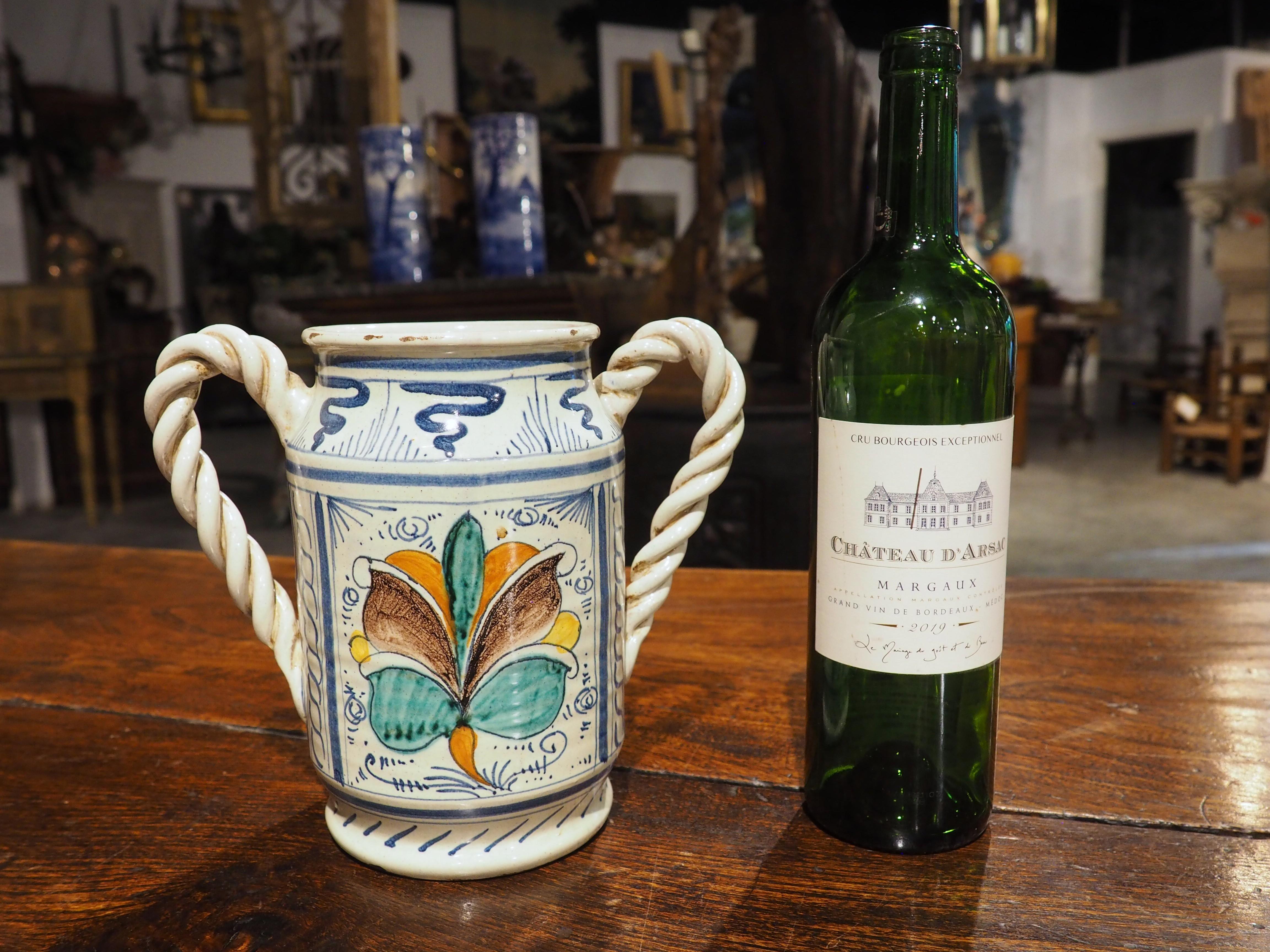 More information coming soon…

A rather unique albarello jar from Italy, this handled majolica drug vessel, which dates to the 1800s, has colorful, hand-painted cartouches on a white ground.  One cartouche depicts a large flower, while the opposing