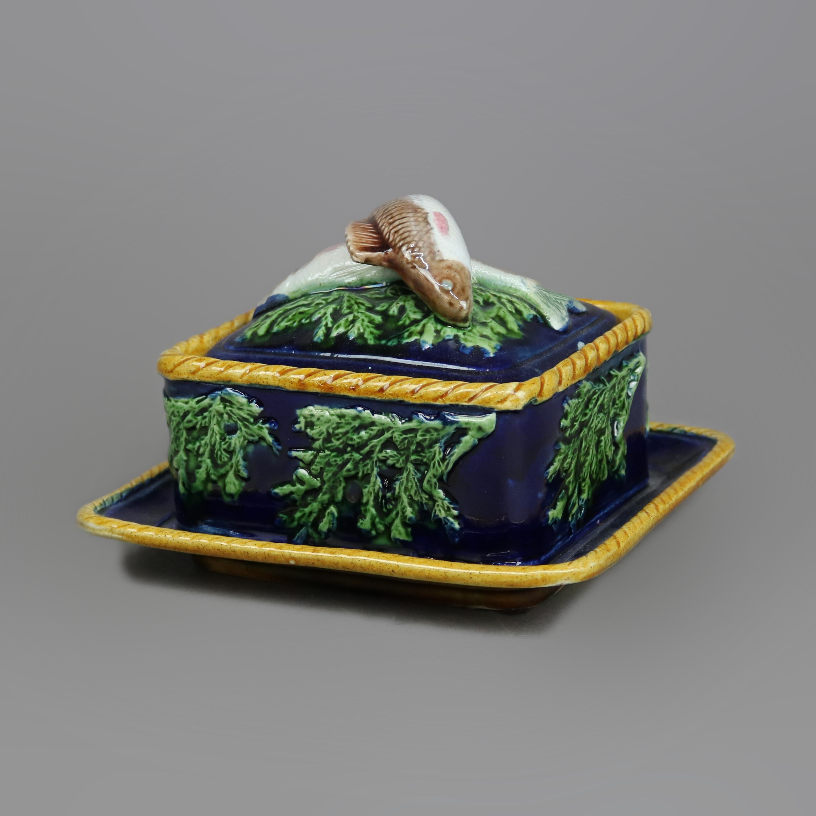 An antique English Majolica sardine box by George Jones offers pottery construction with figural cover having sardine form handle over cobalt blue glazed lid with seaweed leaves in relief and rope twist border, seated on matching under tray, 19th