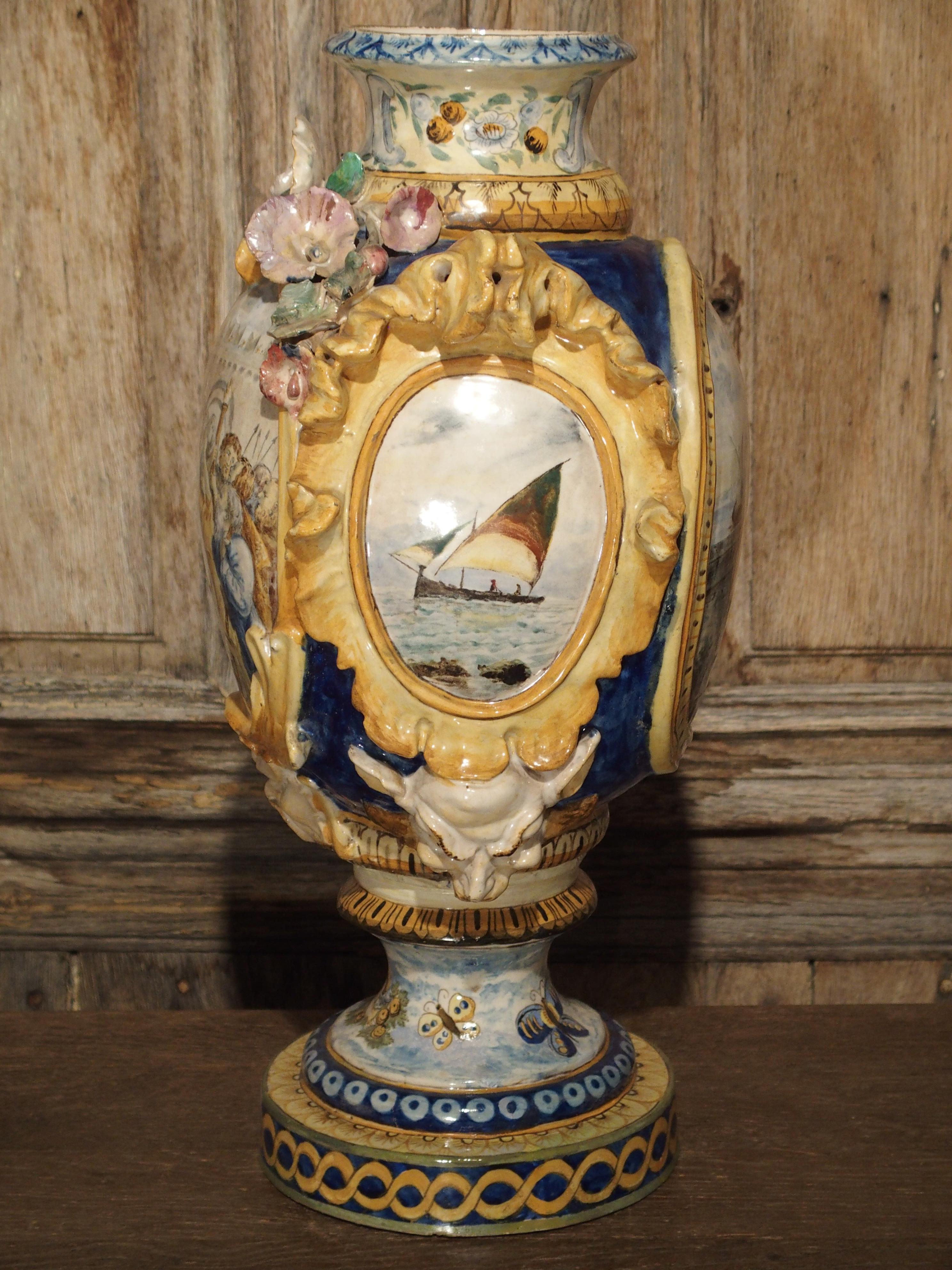 From Italy, this bright Majolica vase has colors of yellow, blue, gold, white and more. Each side of the vase has hand painted scenes with motifs of butterflies, cherubs, flowers, animals, and more. There are gros relief forms of shells, flowers,