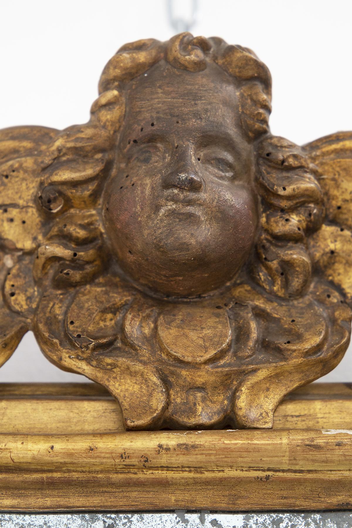 Antique Italian wall mirror made of carved and gilded wood. At the centre of the wooden frame we find carved a putto's face. 17th century. The beauty of this marvellous mirror is also given by the slightly eroded mirror glass due to age and use. The