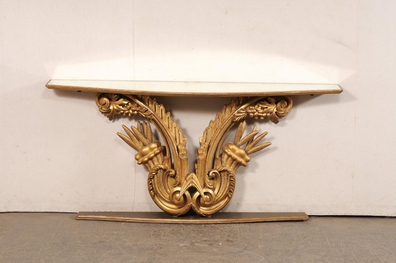 An Italian cornucopia motif carved and gilt wood wall console with mirrored top from the early 20th century. This antique table from Italy features its original mirrored glass top (with beautifully bowed shaped), which is raised upon an