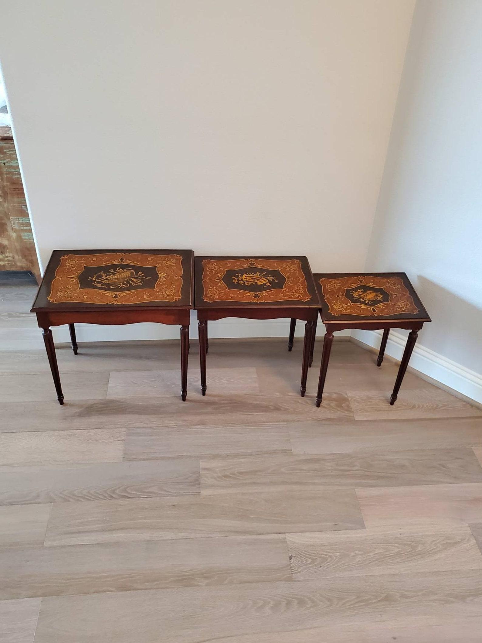 A beautiful nest of three Italian mahogany marquetry inlaid tables from the late 19th - early 20th century. The trio of antique tables feature finely detailed marquetry inlaid tops with wonderful musical instruments, flower and foliate decoration in