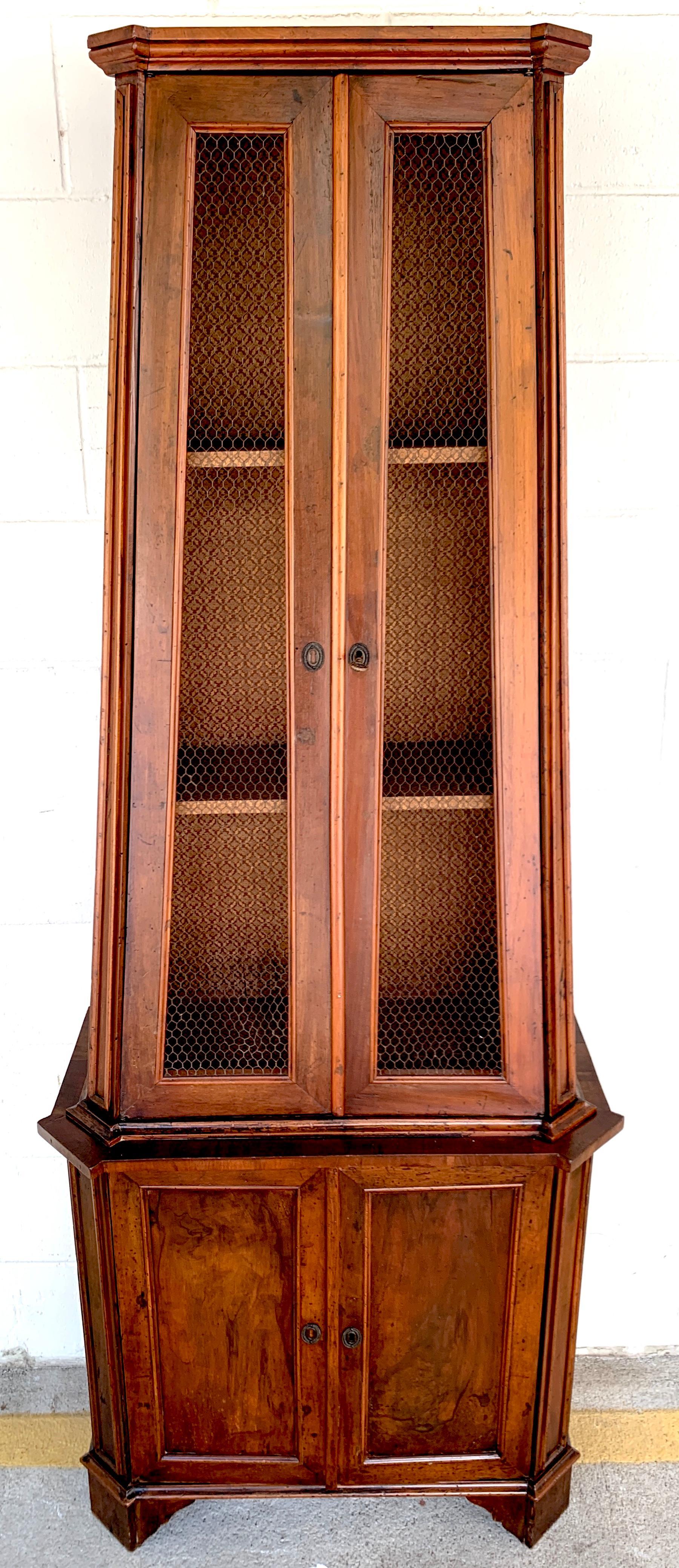 Ancienne armoire pyramidale italienne néoclassique en bois d'olivier, en deux parties, la caisse supérieure effilée avec un intérieur à étagères, et des portes à mailles en laiton, avec clé. La caisse inférieure à panneaux est équipée de deux portes