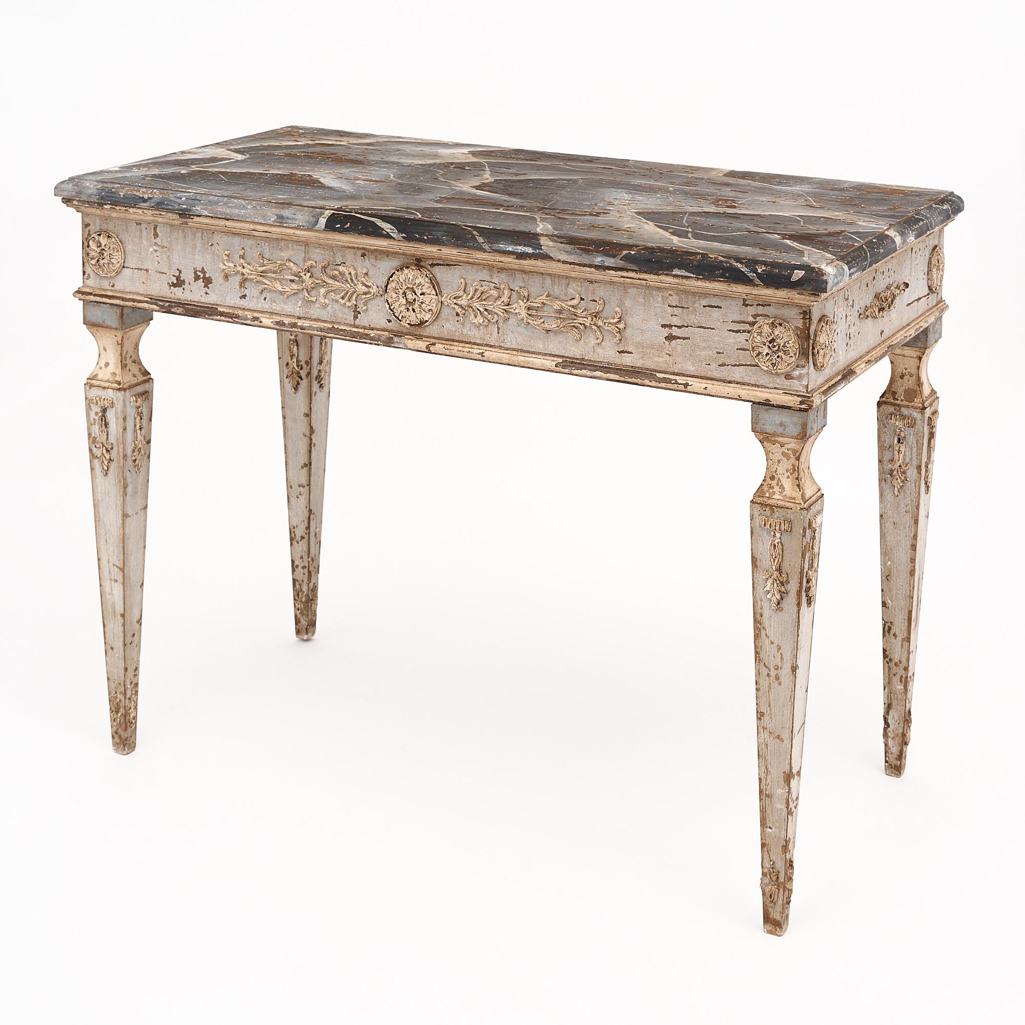 Pair of consoles from Italy featuring hand-carved floral friezes and tapered legs. The bases of the tables have a soft Trianon gray color. The tops are hand-painted with a faux marble finish.
