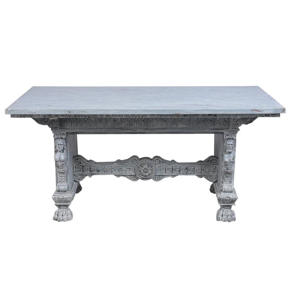 This antique Italian Renaissance dining room table is made out of walnut wood and newly painted a pale gray and off white color with a distressed finish. This dining table features a wooden top with detailed moldings and heavily carved wood accents