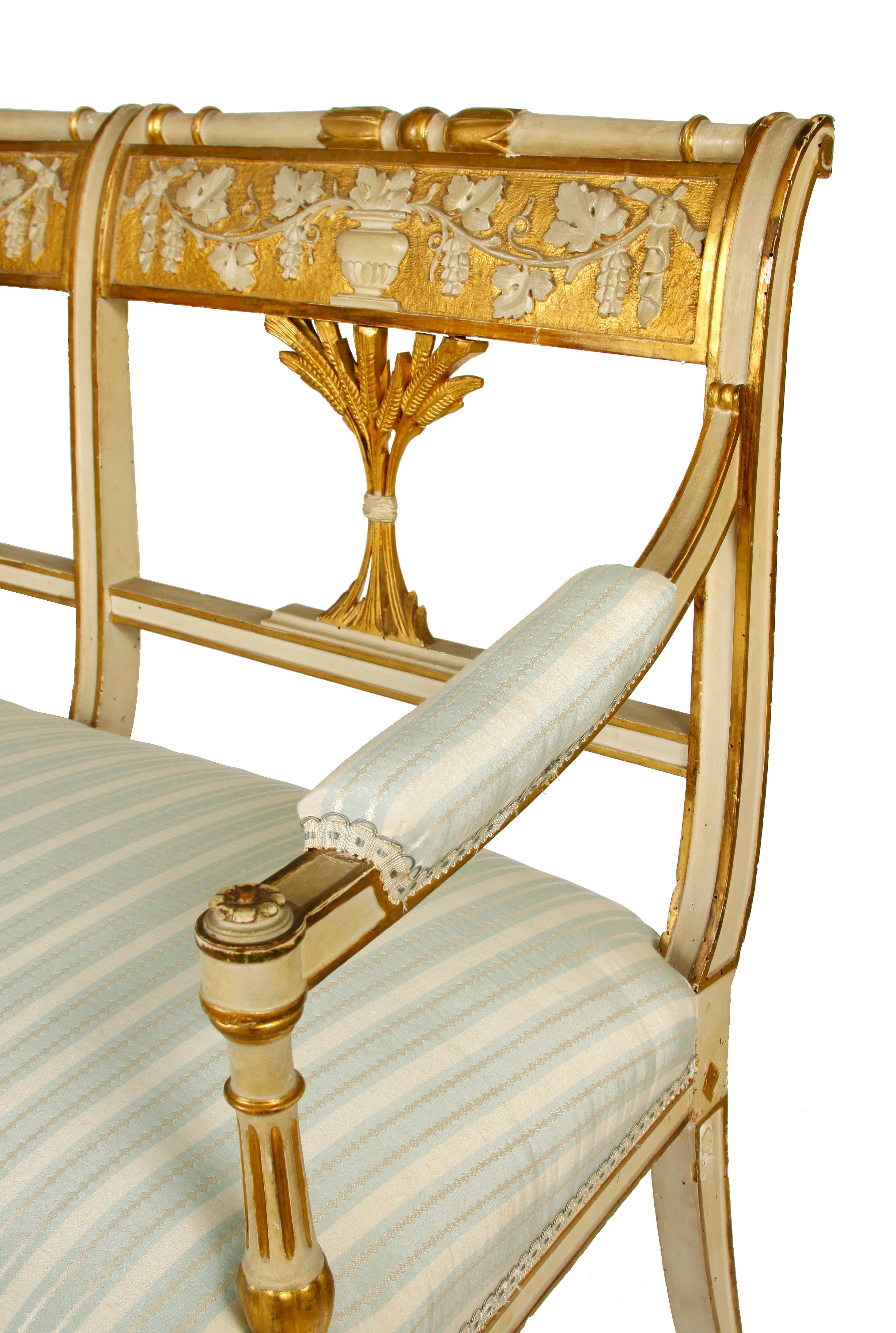 Antique Italian painted and gilt settee. Louis XVI style circa 1900 with carved back depicting wheat, grapes and vines. Newly reupholstered in blue and cream striped fabric.