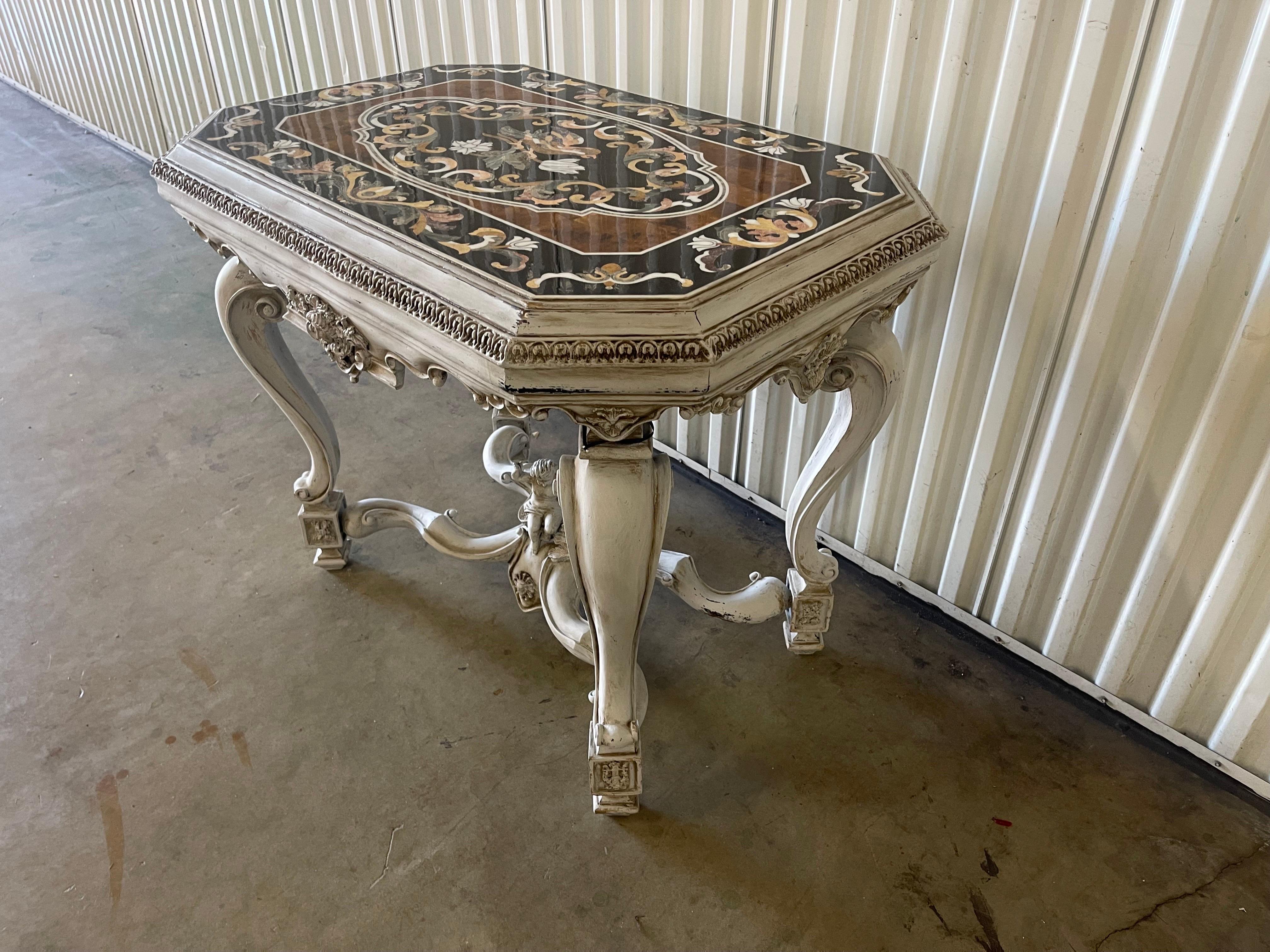 Carved and painted Rococo style center table with pietra dura top. Carved and gesso base with putto in center. Legs are in the cabriolet style.