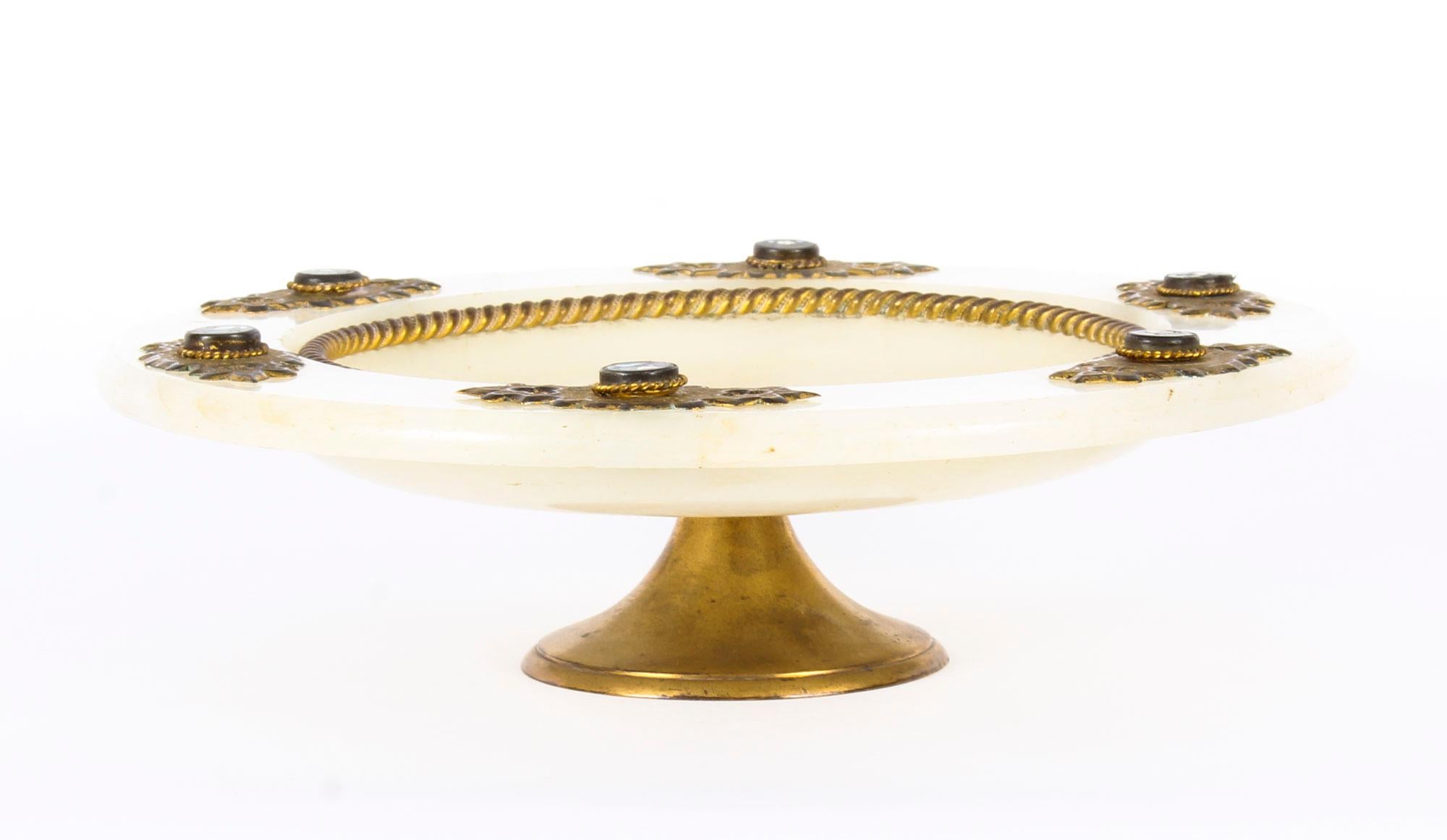 Si tratta di un antico piatto da portata in pietra dura, ottone dorato e alabastro, risalente alla fine del XIX secolo.

Con una straordinaria montatura in ottone cesellato in stile neogotico, questo splendido piatto in alabastro è incastonato con