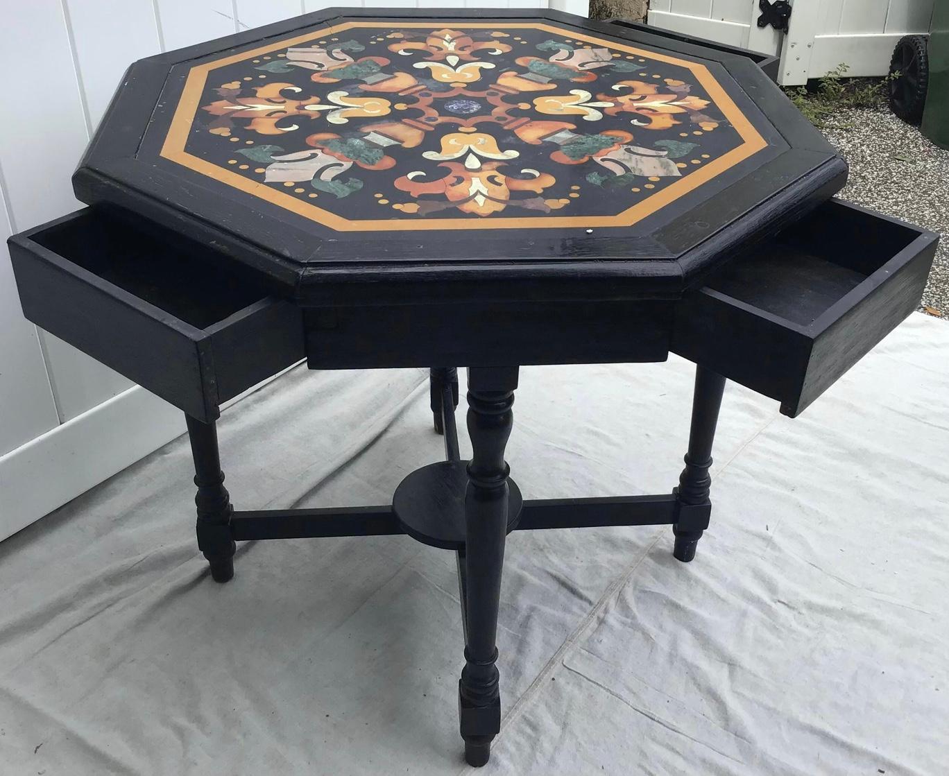 Raffinato tavolo ottagonale in pietra dura intarsiata del XIX secolo, con base ebanizzata e quattro cassetti. Il piano intarsiato in pietra dura raffigura un disegno stilizzato con intarsi in marmo colorato, tra cui lapislazzuli e pietre colorate,