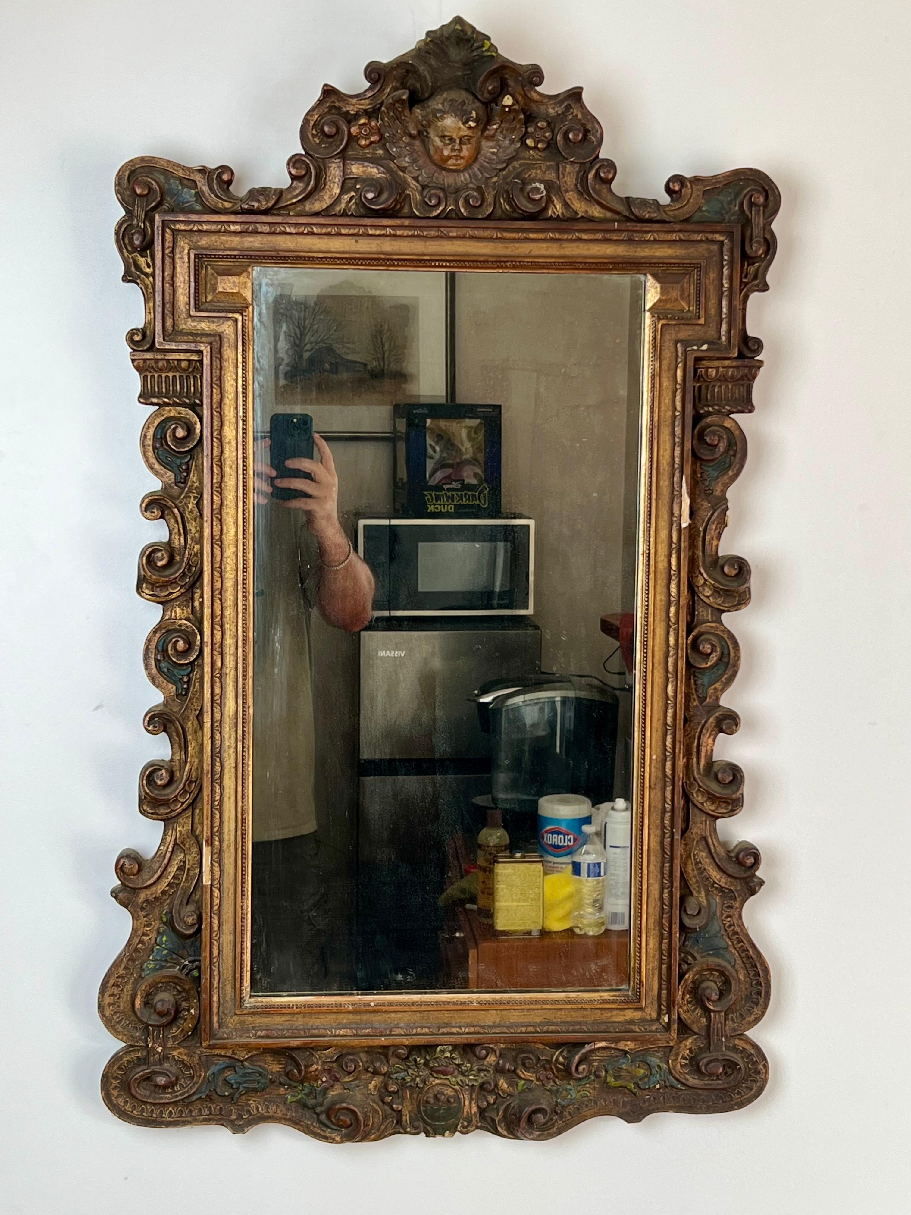This stunning antique Italian wall mirror captures the opulence and artistry of the Regency style, featuring a deeply carved giltwood frame adorned with scrollwork, acanthus leaves, and a central cherub crest. The craftsmanship is remarkable, with