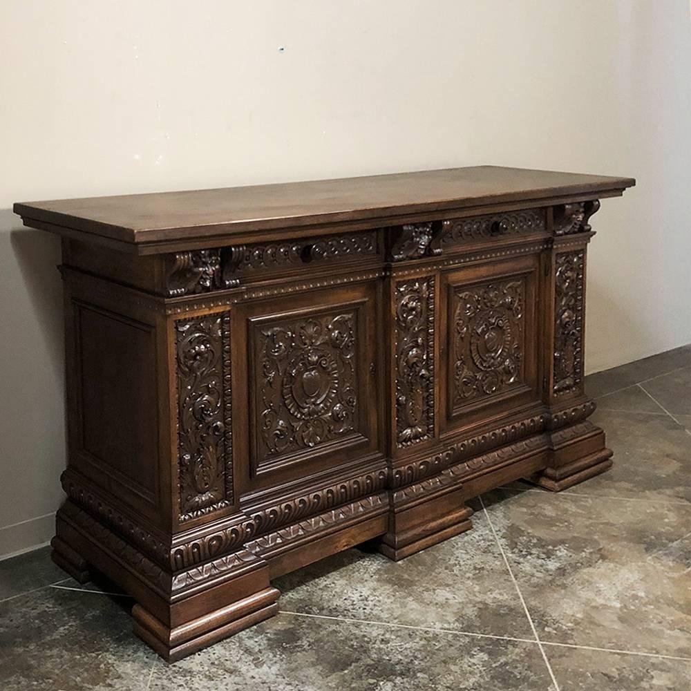 Antique Italian Renaissance hand-carved walnut buffet features elaborate relief carved into each of three large door panels surrounded by bold molding, carved drawer facades, and carved pilasters with foliate motifs. It rests on a massive pediment