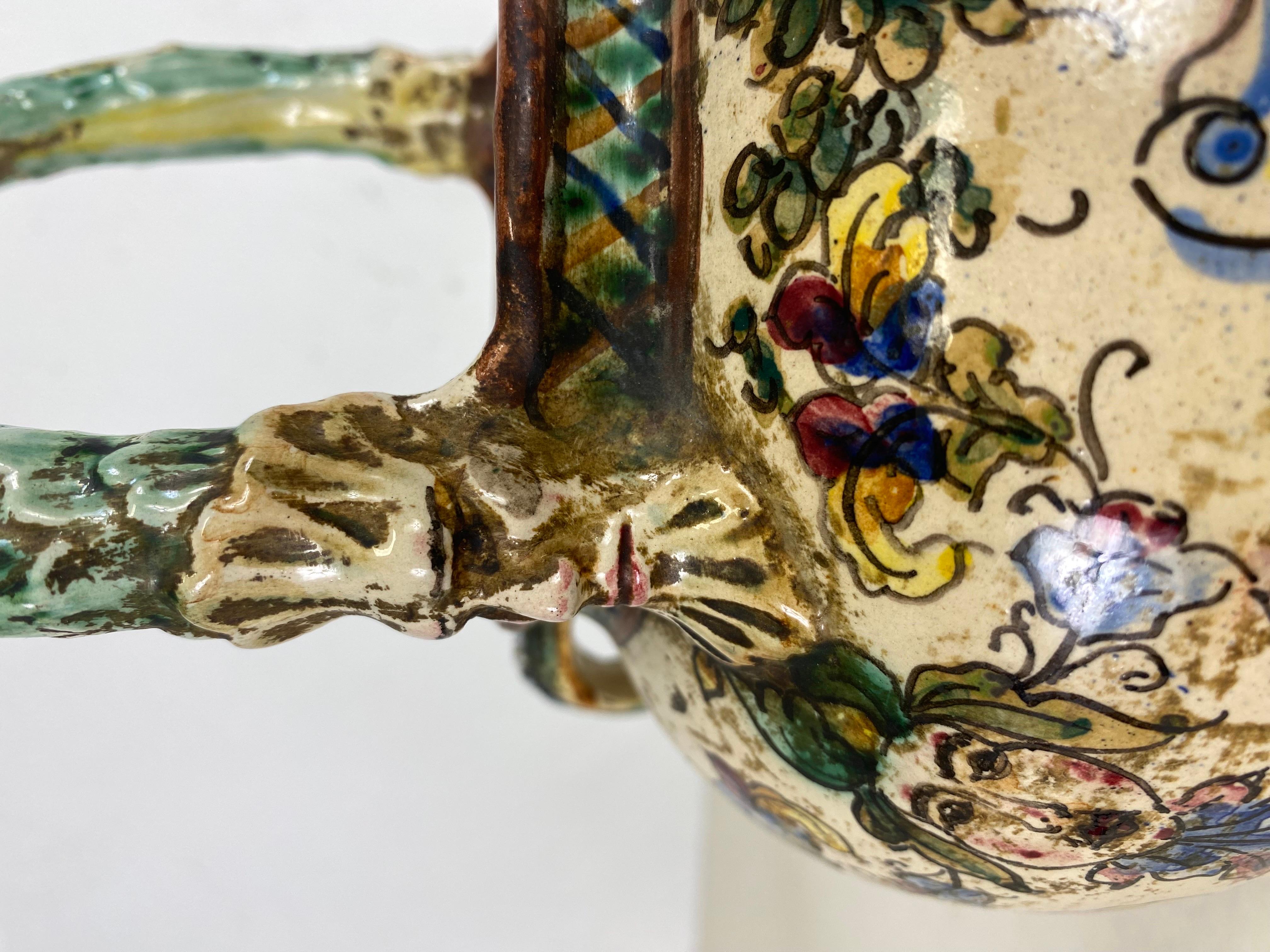 This is an Italian renaissance revival ornately decorated terra-cotta pitcher. This vessel features extraordinary hand-painted figures and flora around the entire surface of this piece. Beautiful tones of vibrant blue, green, yellow, and red. This