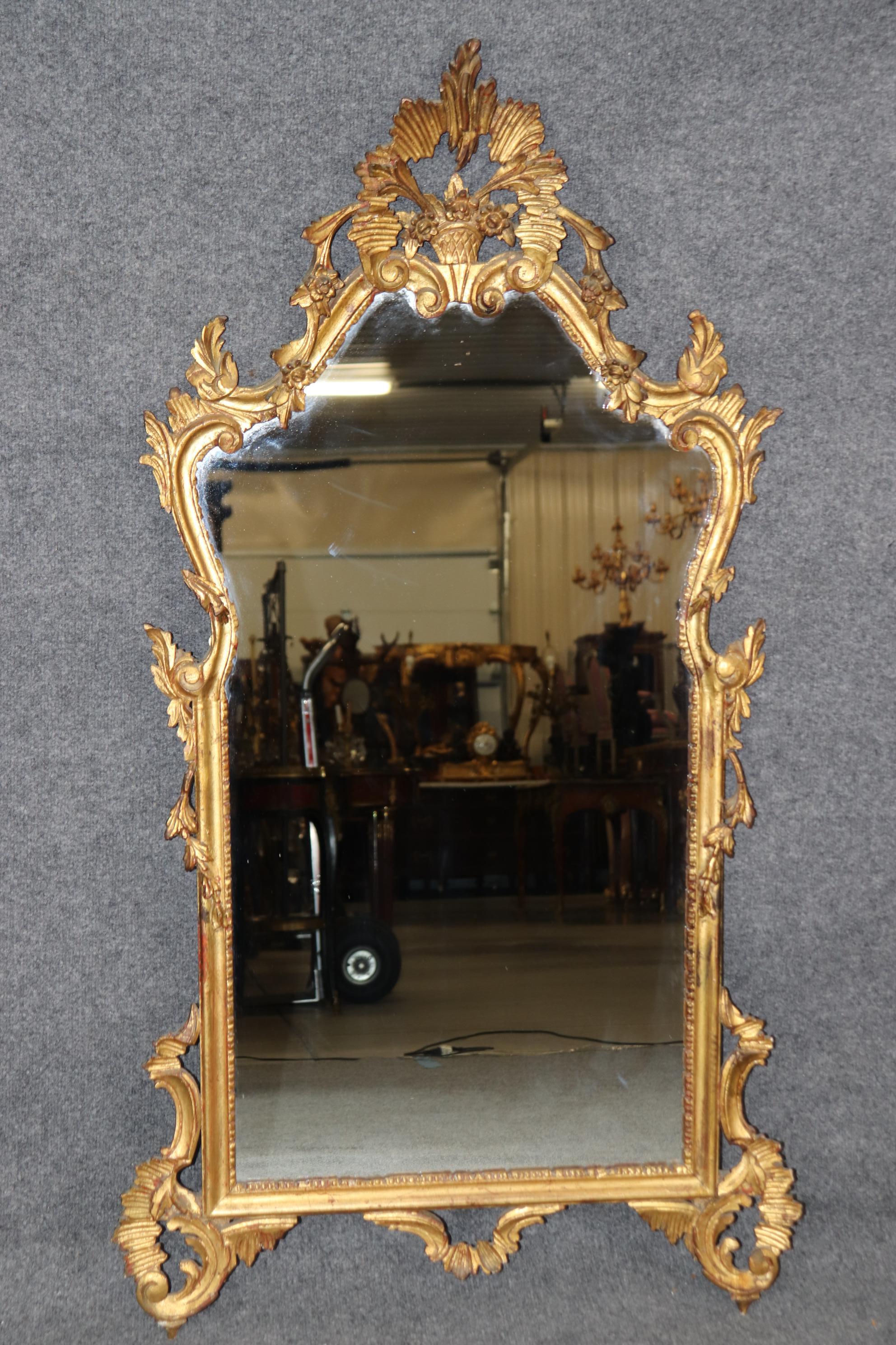 Abmessungen - H: 52 1/4 in B: 29 in T: 4 in 

Dieser exquisite antike italienische Rokoko-Spiegel mit vergoldeten Schnitzereien an der Wand strahlt zeitlose Eleganz und Handwerkskunst aus. Die aufwändigen Schnitzereien mit den geschwungenen Kurven