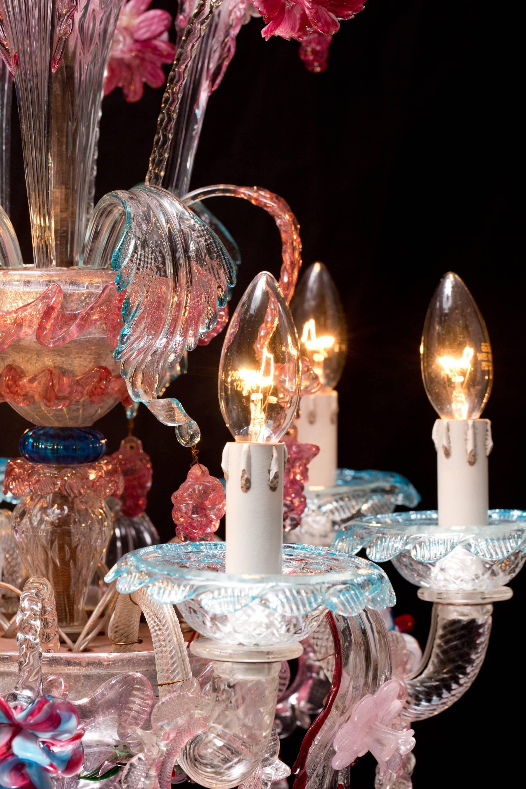 A unique antique Italian chandelier made from Murano glass from Venetia. The chandelier has six swingled arms with a light bulb at each end of the arm. Between each arm are colored flowers and leaves. At the second level in the middle of the
