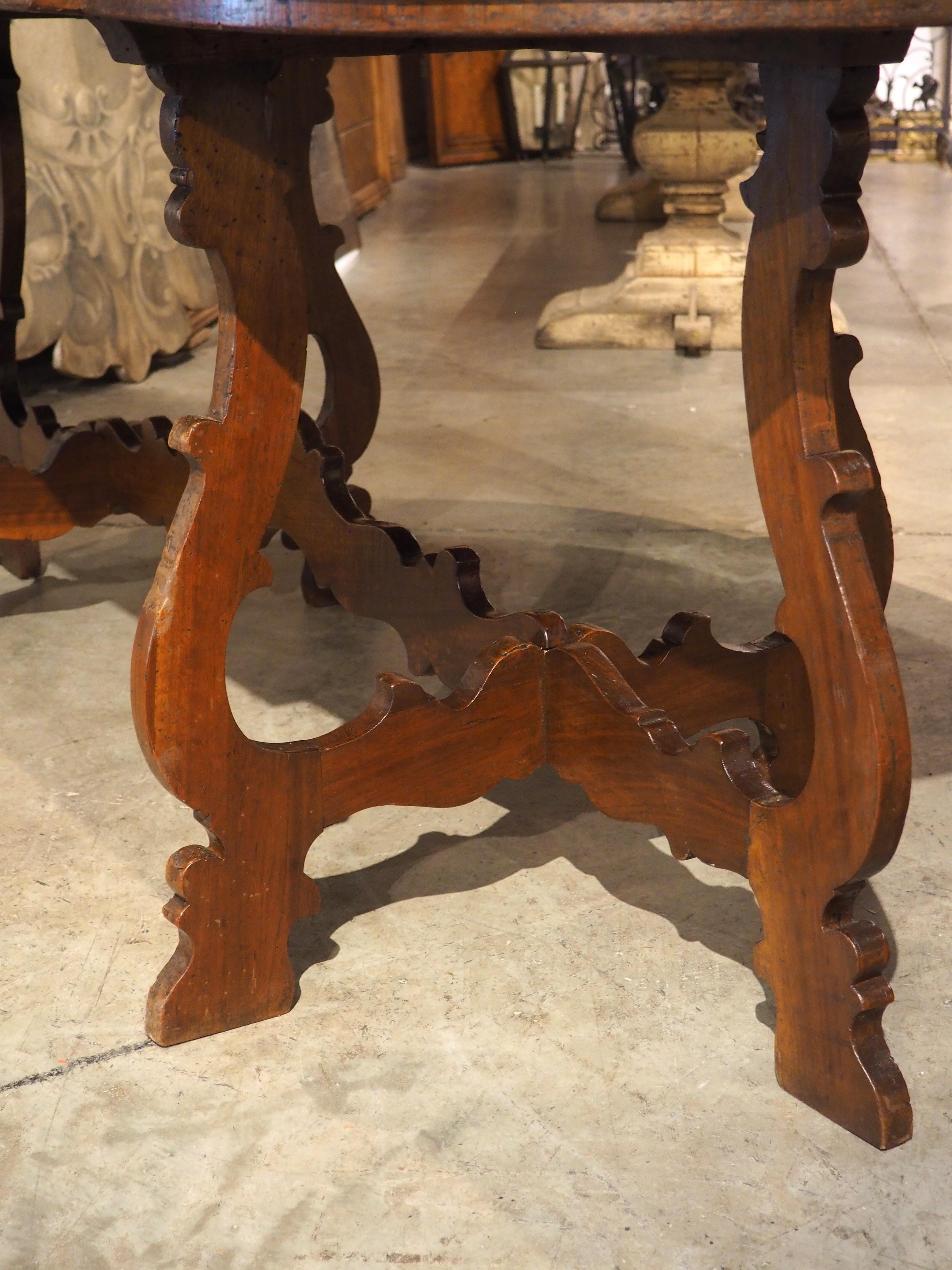 Dieser Tisch aus Nussbaumholz ist eine einzigartige und faszinierende Variante der traditionellen italienischen Leierbeintische. Er verfügt über ein drittes Bein, das gleichzeitig als Bahre dient. Die um 1860 handgeschnitzte, leicht vertiefte,