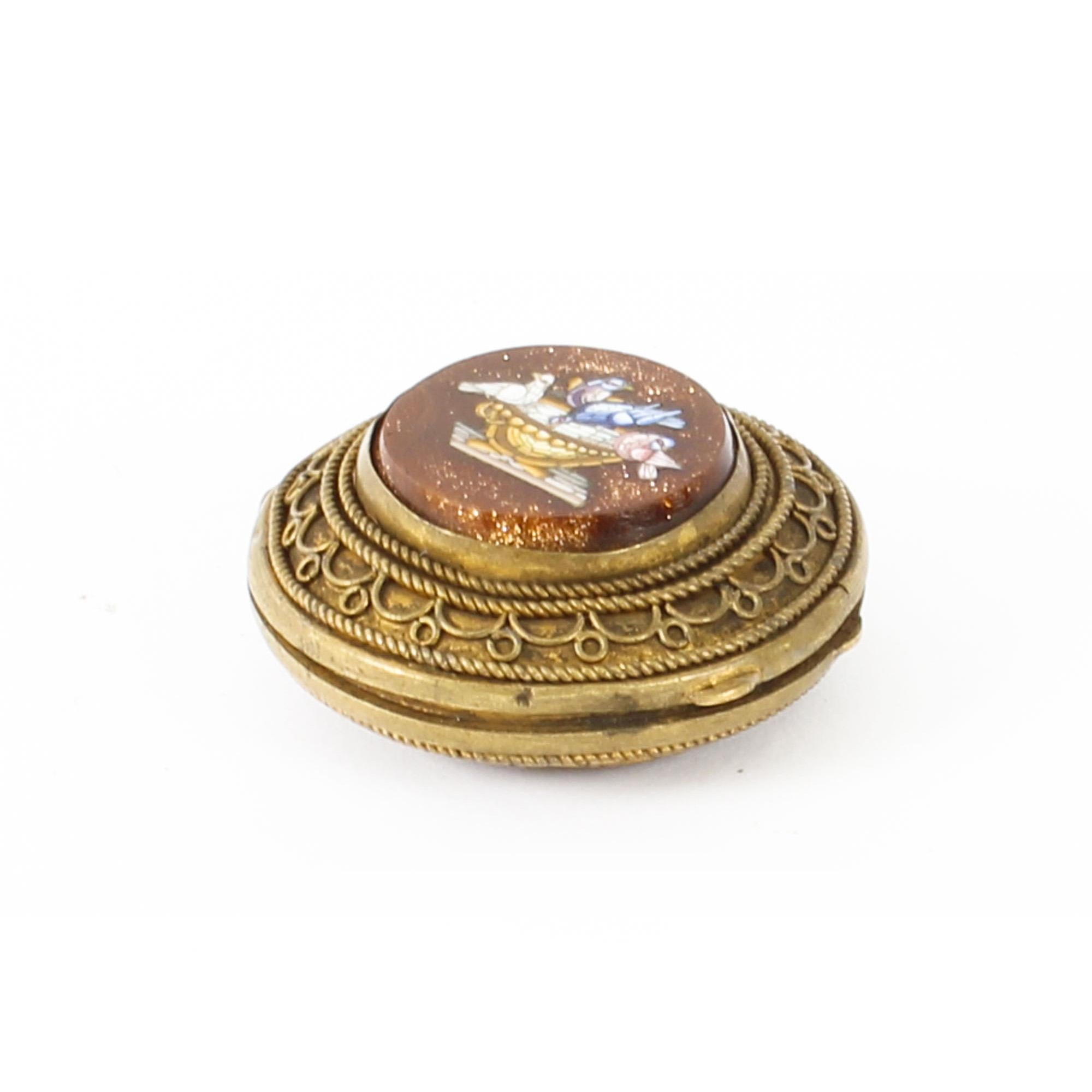 This is an exquisite antique Italianate ormolu pill box with two micromosaic plaques, dating from the late 19th century.

The box is hinged and round in shape. The top of the box is decorated with a charming centred and raised micromosaic of
