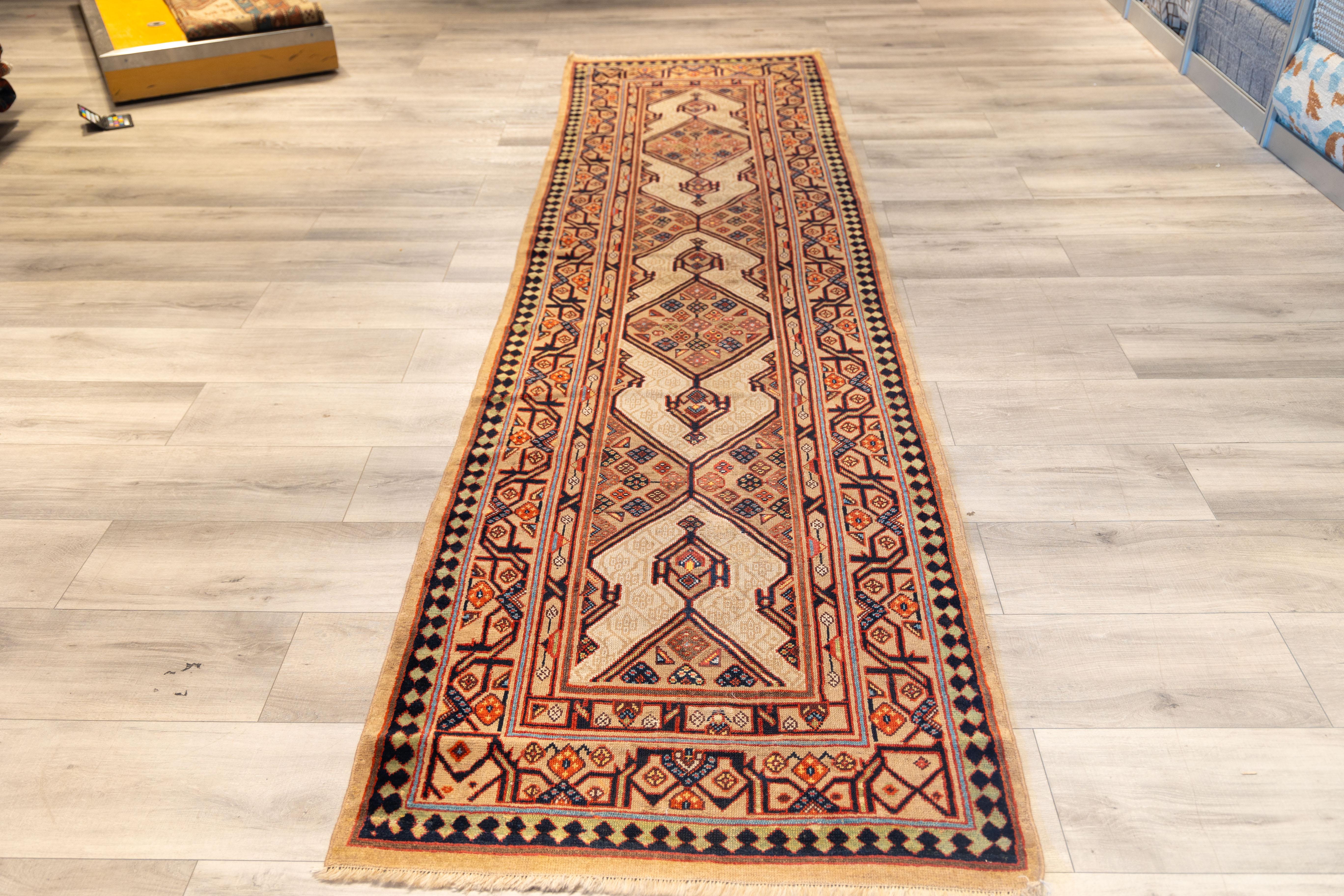 Bakshaish runner featuring a soft beige background with a repeating diamond medallion pattern in salmon, rust, and charcoal. Each diamond holds small, geometric floral details, giving the rug a balanced rhythm. The border combines warm reds, pinks,