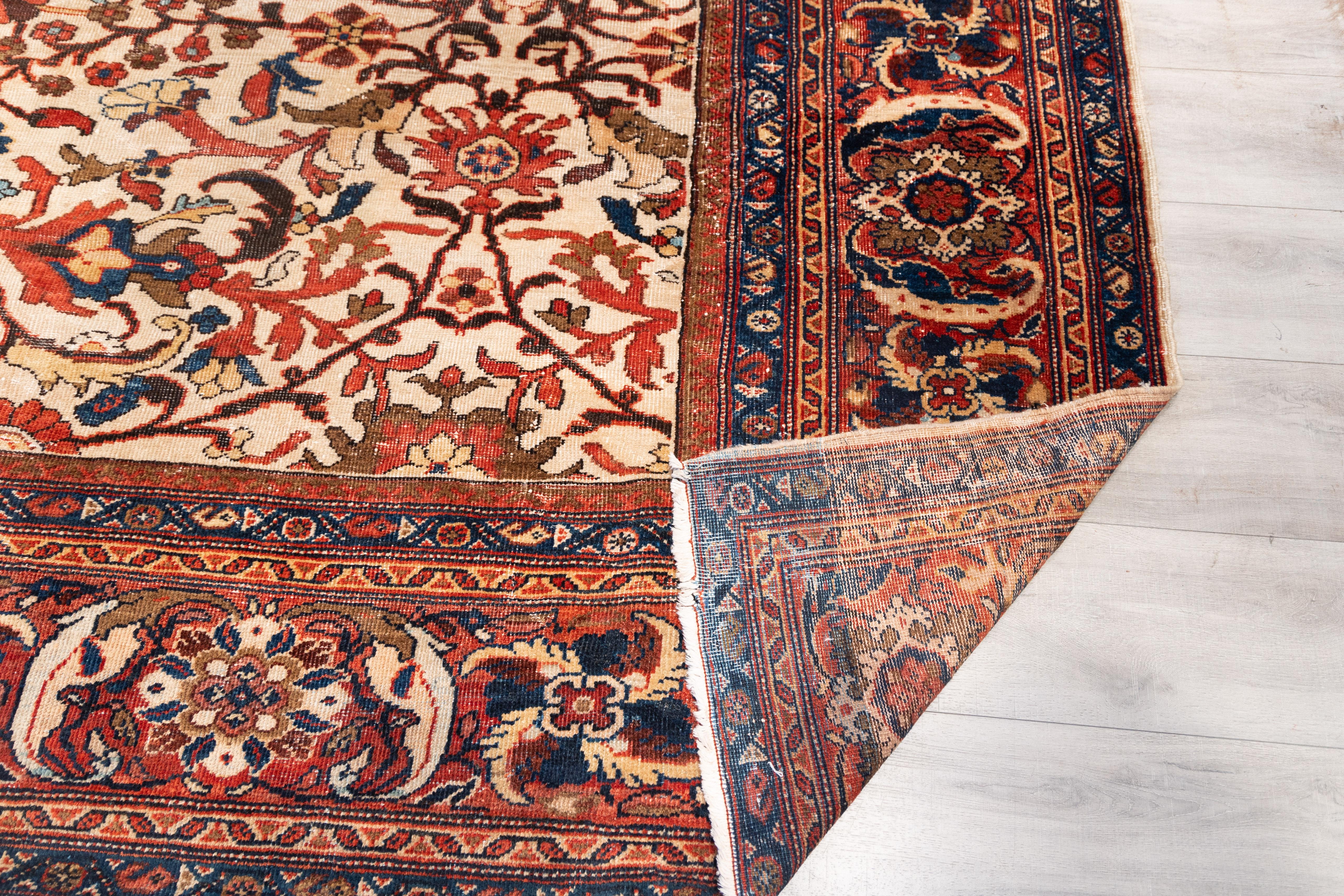 early 20th-century Mahal carpet presents a striking allover arabesque pattern centered on a cream ground. The field is filled with scrolling vinery, serrated leaves, and palmettes in rust red, navy, ochre, and forest green. The symmetrical design is