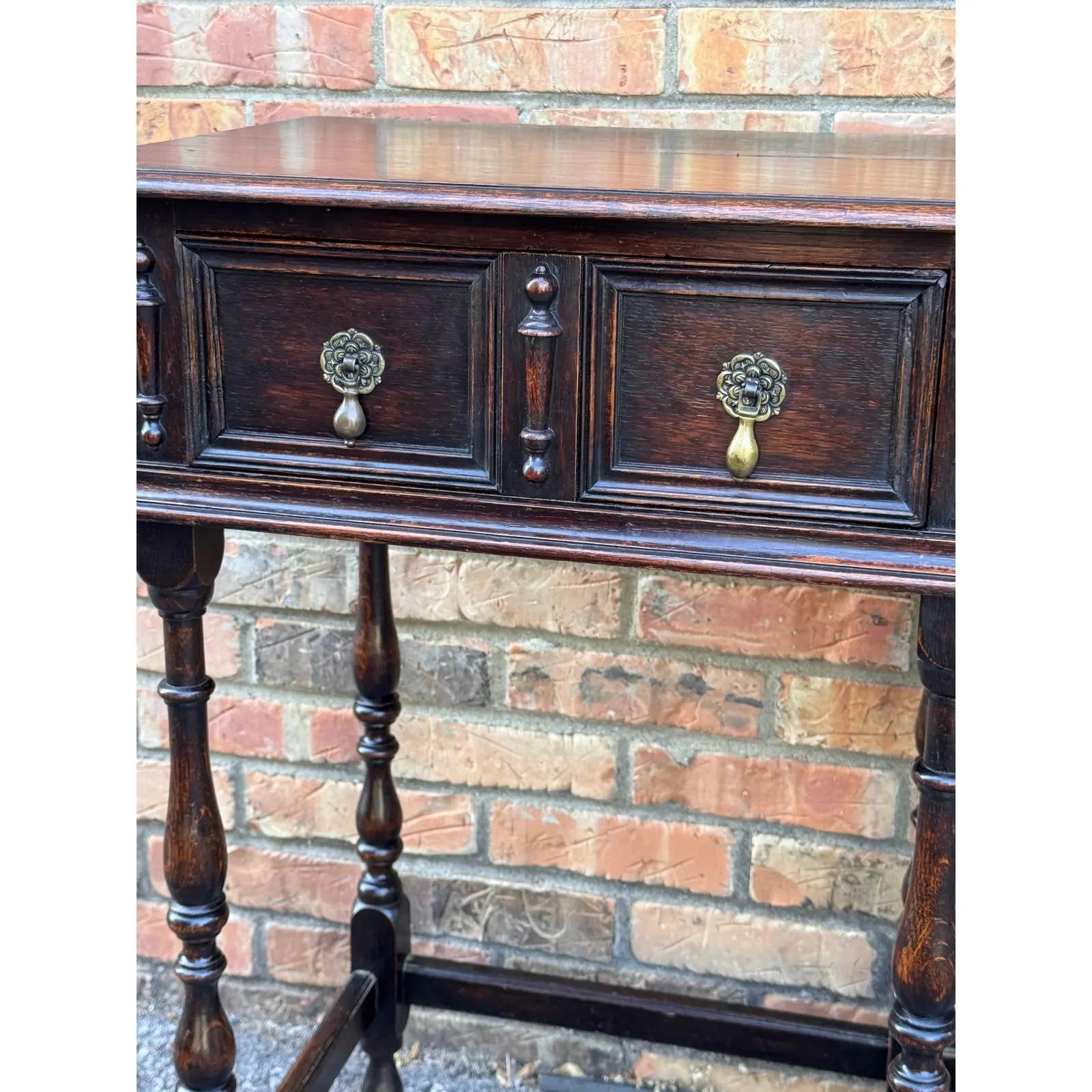 This small antique Century Jacobean console table features rectangular top over carved drawers, adorned with lovely drop pulls. The apron has filigree motifs and turned legs anchored by stretcher bars. This table is a versatile size for the small