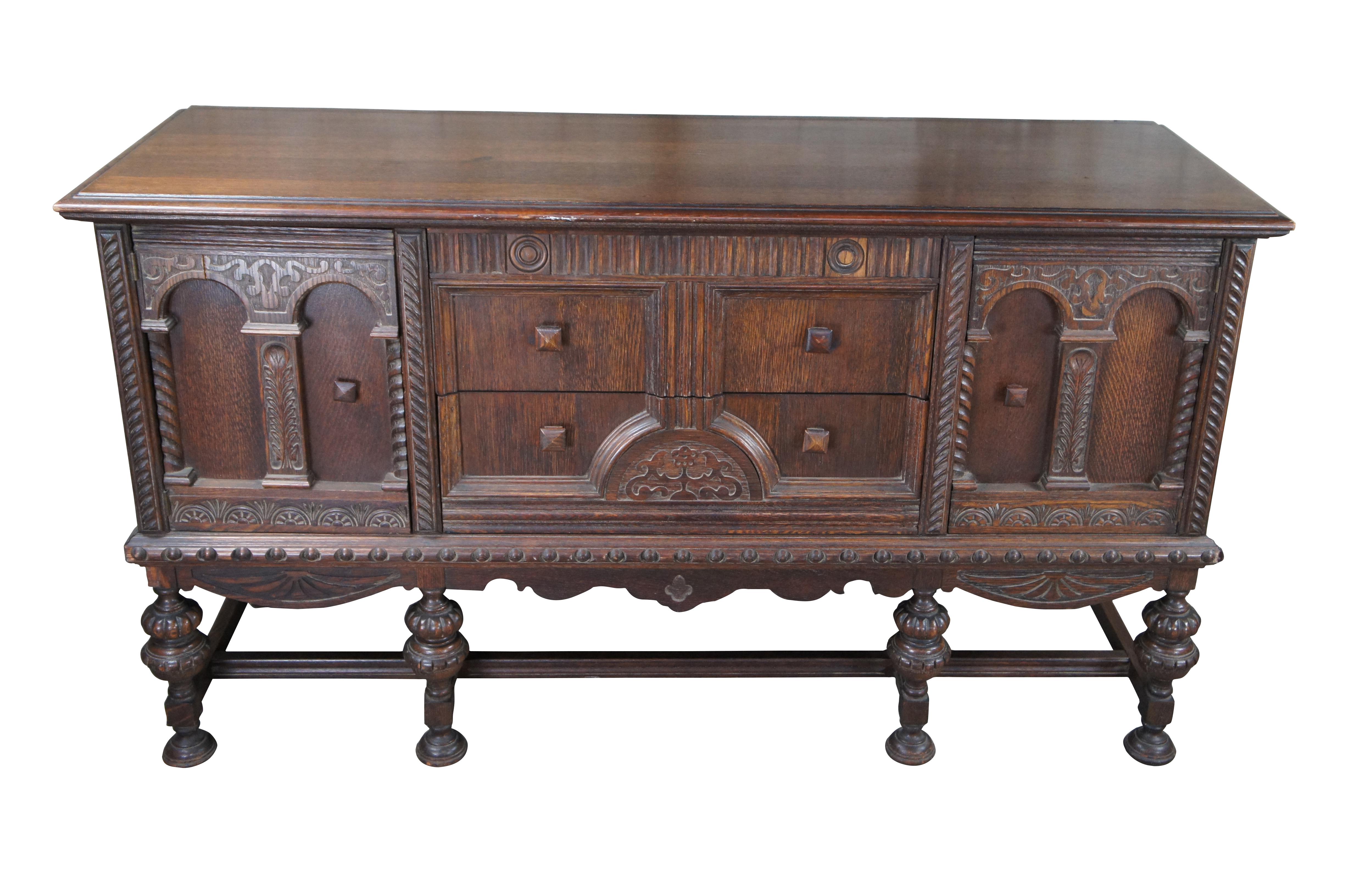An antique Jacobean style buffet, circa 1930s. Features a rectangular frame carved from oak with three central dovetailed drawers flanked by outer cabinets for accessory storage. Uppermost drawer is concealed / hidden and requires the second drawer