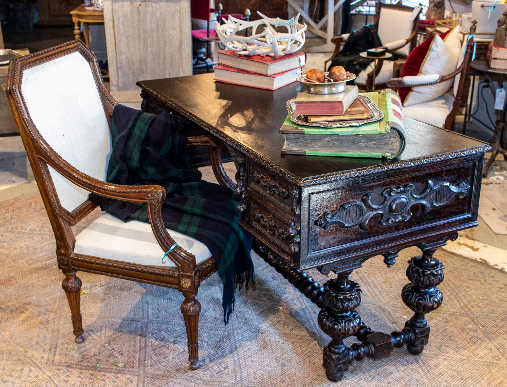 This is an antique Jacobean revival styled desk with four drawers and beautifully carved details. The edge of the top of the desk is hand carved along with the front and sides, with palmettes and floral carvings. The legs are beautifully turned in