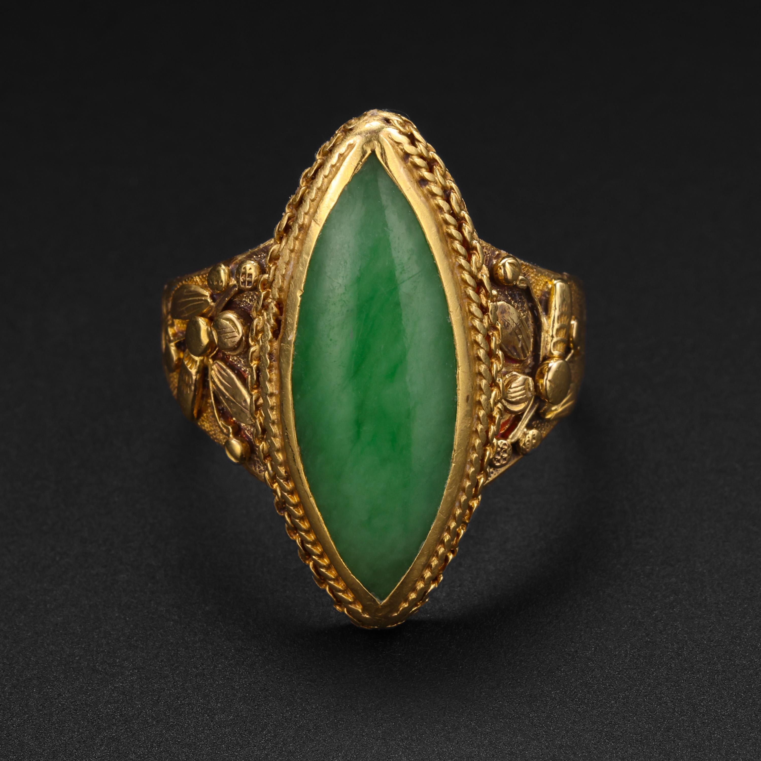 Created in rich, buttery 18K yellow gold and jade, this ring was created by hand near the end of the 19th century in China. Featuring elaborately carved shoulders depicting highly detailed flowers. The goldsmithing is quite impressive. 

Bezel-set