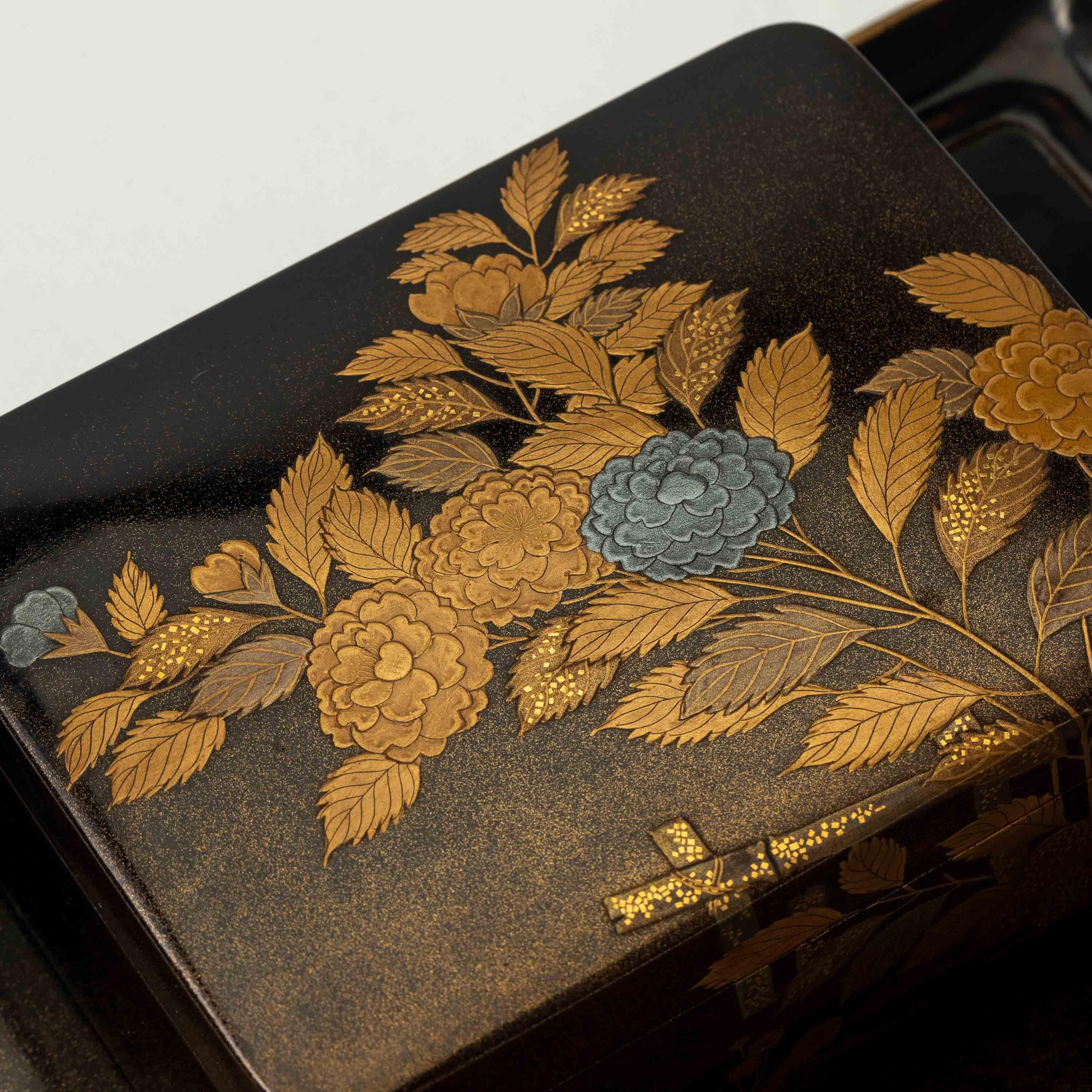 Antique Japanese black lacquer cigarette box on a tray. It has a delicate design of flowers and flowing water in gold and silver maki e, on a nishiji lacquer background. Nishiji is a lacquerware technique that produces a finely speckled effect,