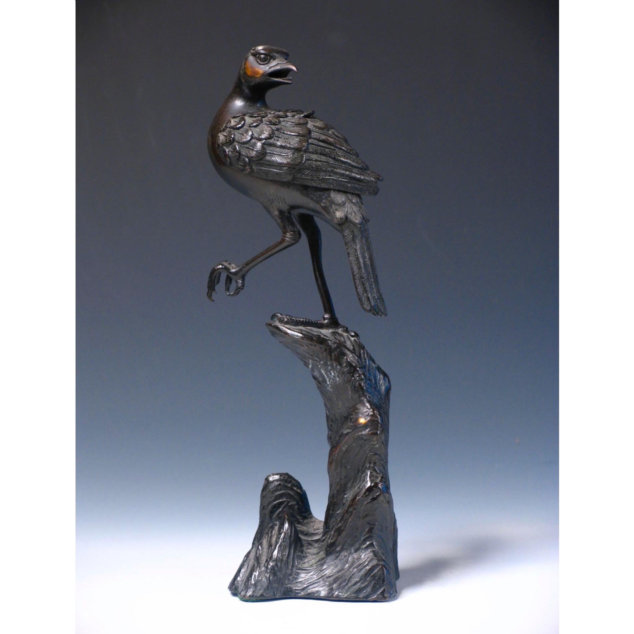 Antique Japanese bronze incense burner, in the form of a bird perched on one foot on a tall rocky outcropping, the bird’s head looking back with open mouth and pierced removable wings revealing the incense chamber, the left foot partially clenched,