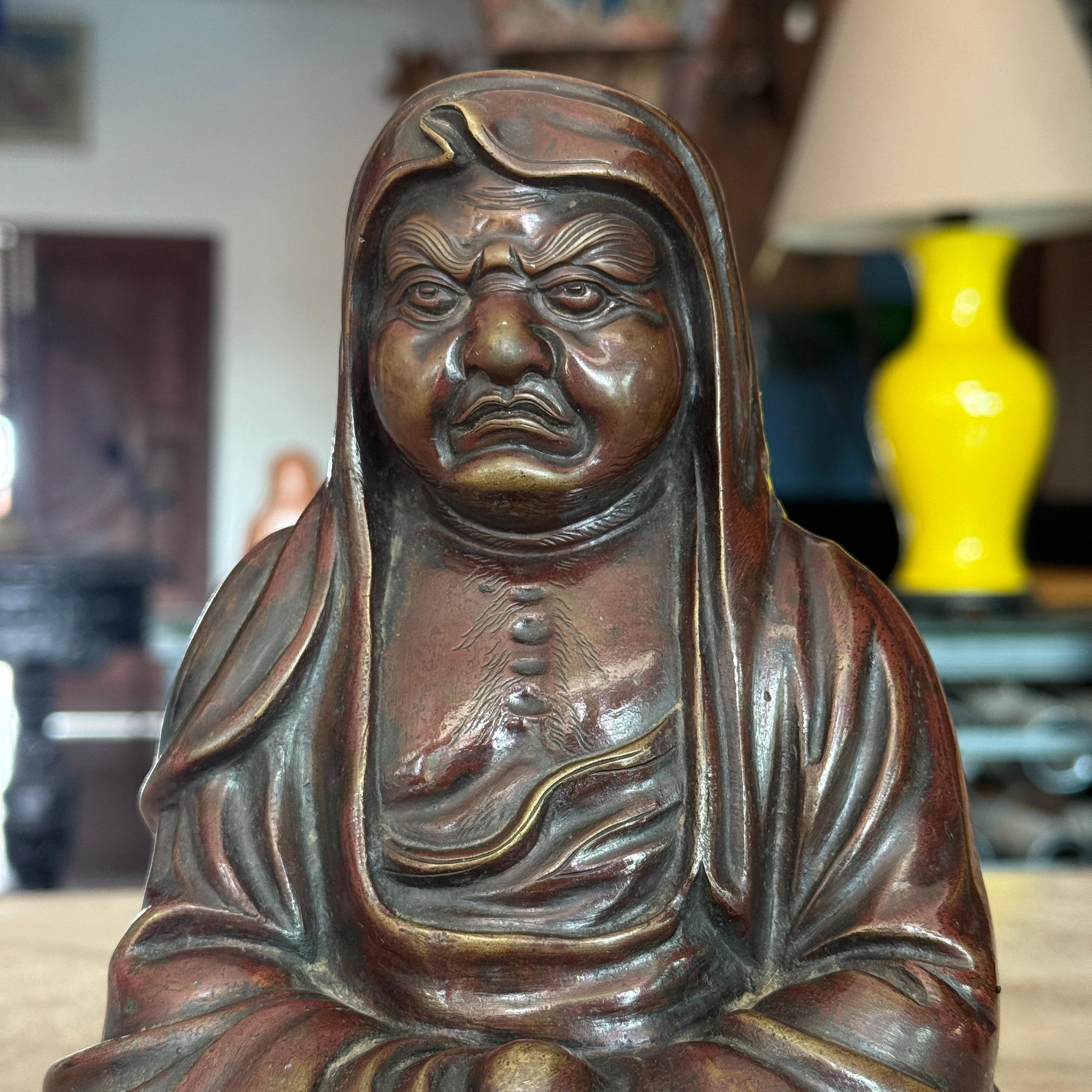 Cette statue Daruma en bronze japonais du XIXe siècle est une représentation saisissante et contemplative de Bodhidharma, le fondateur révéré du bouddhisme zen. Coulée dans le bronze avec un niveau de détail exceptionnel, la figure est représentée