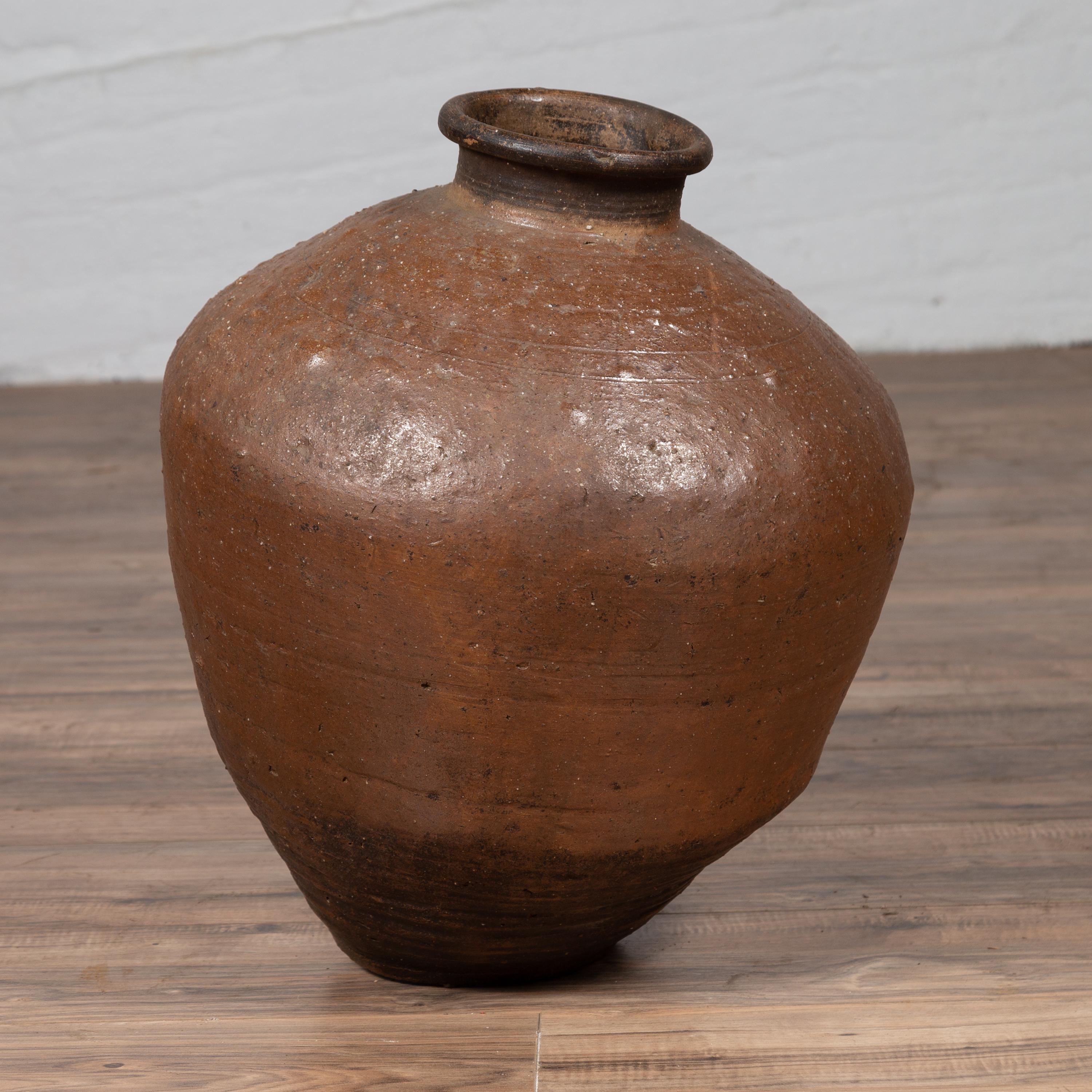 An antique Japanese brown oil jar from the early 20th century, with weathered appearance and irregular shape. Our eye is immediately drawn to the interesting shape of this Japanese oil jar, presenting a brown body with darker accent at the bottom