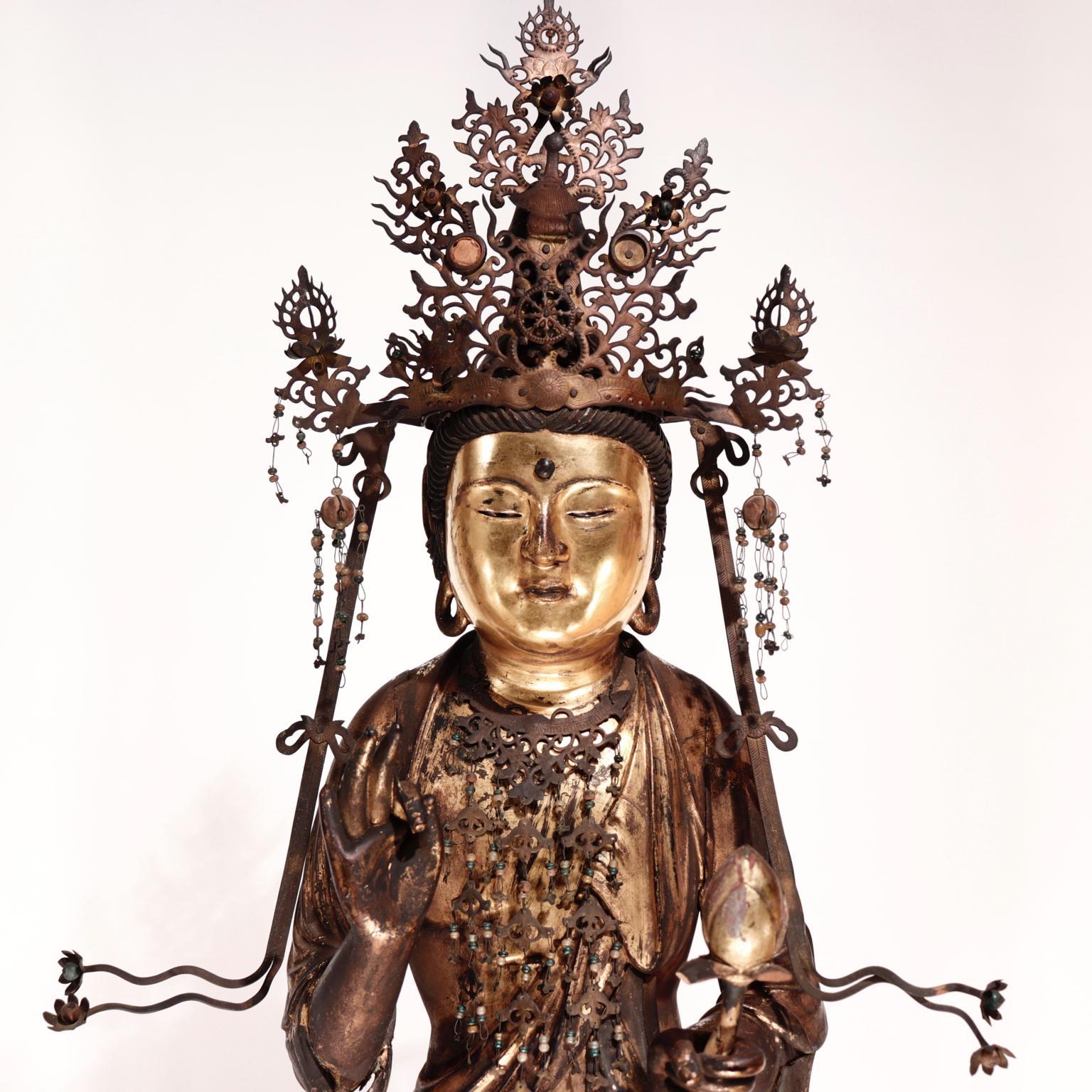 Japanese Buddhist assembled wood sculpture of Kannon-Bosatsu (Avalokitesvara), the God of Compassion, standing male figure with abundant cloak drapery including the pendant wrapped sleeves, standing on a lotus base on a rocky outcropping, the left