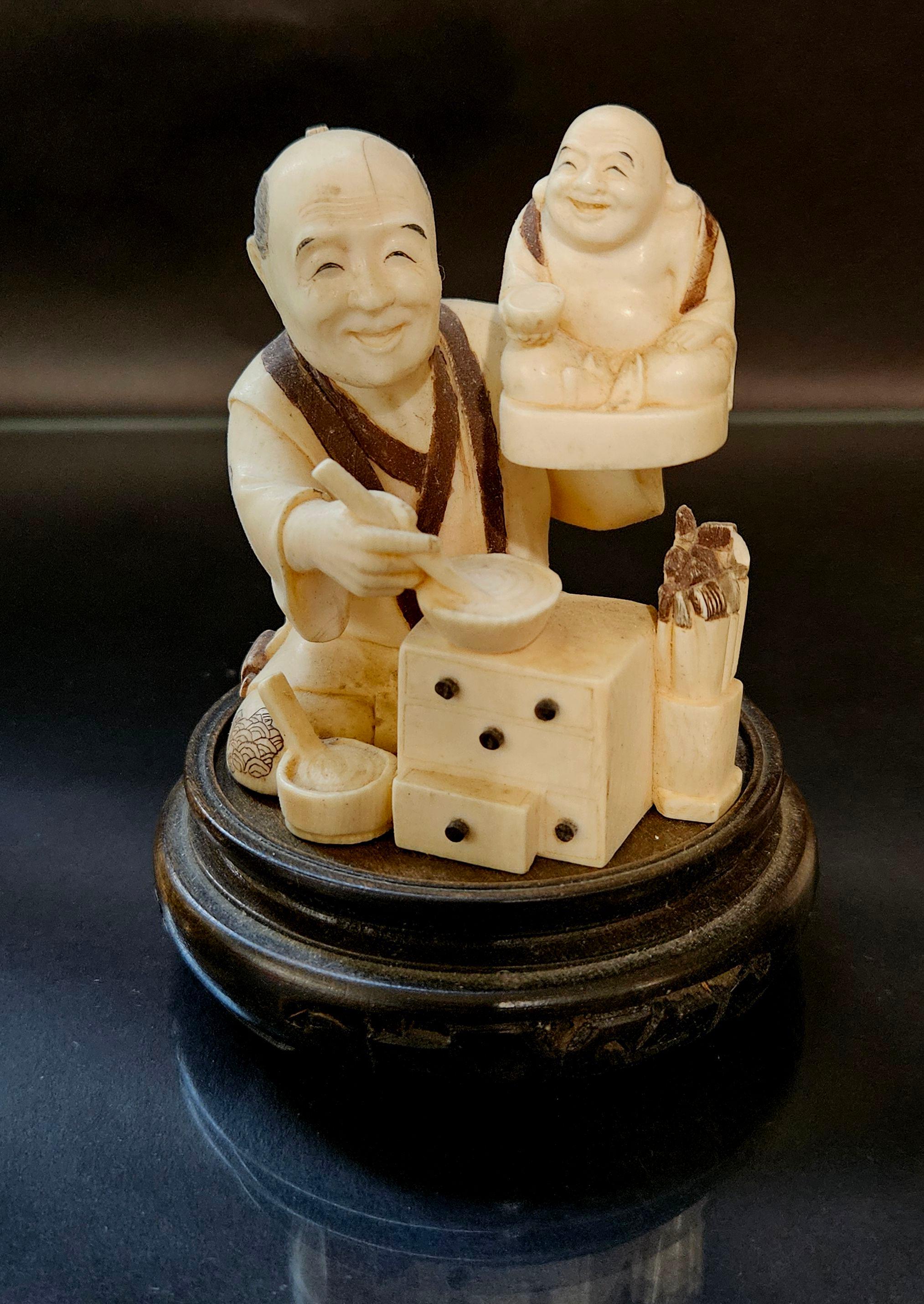 Antique Japanese Carved Okimono Polychrome Decorated Figure Group seated on a wood stand, signed by Gyokko,  depicting a seated artisan carving and decorating a figure of a happy Buddha, having tea-stained accents and signed to the underside, raised