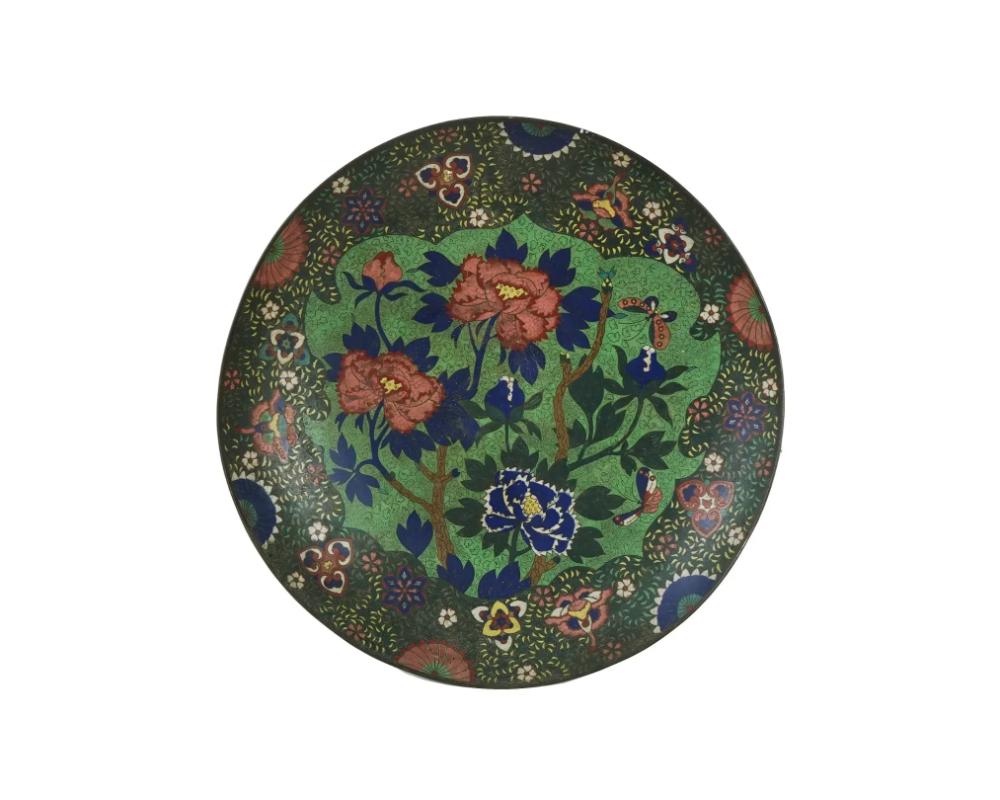 A large antique Japanese enamel over copper serving plate. Early Edo period, 19th century. Footed round dish with elevated rims. The interior of the plate is adorned with a medallion depicting butterflies in blossoming flowers surrounded by floral,