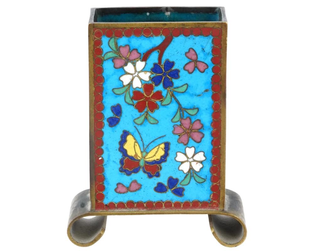 The exterior of the ware is covered with polychrome enamel floral, foliage, and butterfly motifs framed by a geometrical ornament against a bright turquoise background made in the Cloisonne technique. The ware is adorned with openings on the sides.